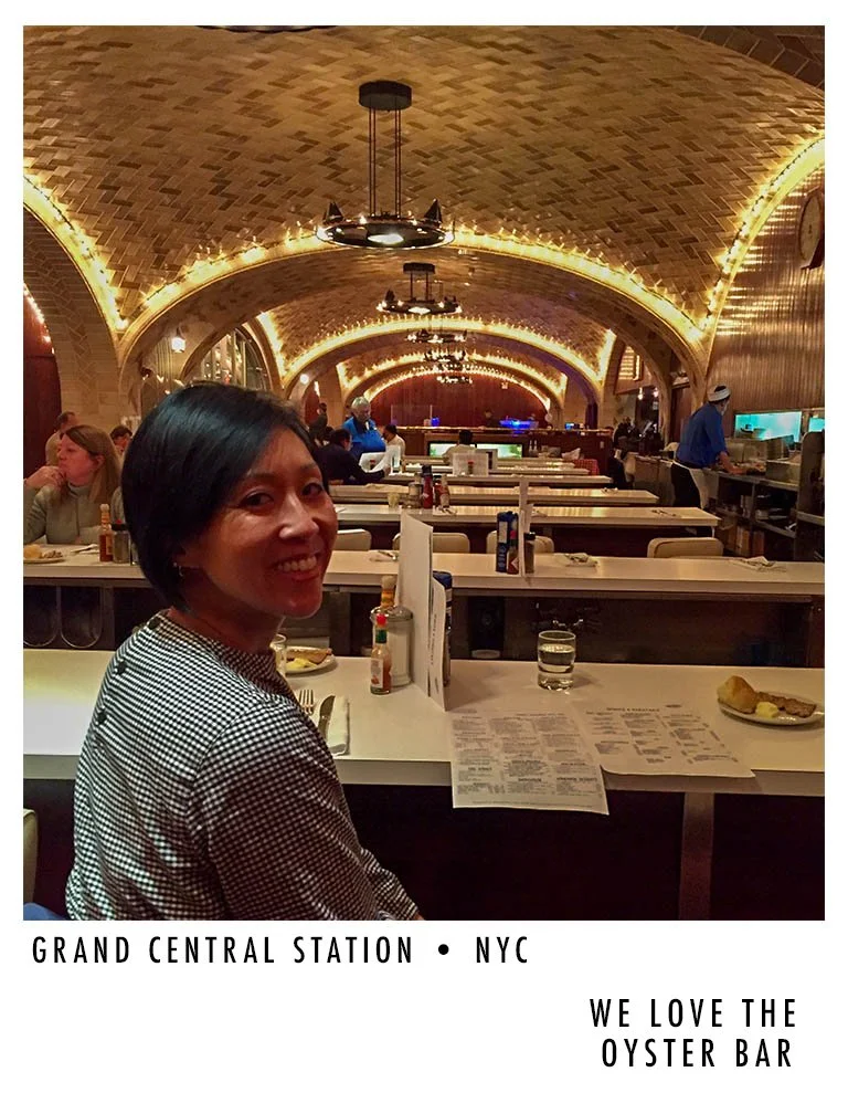 Woman sitting at a bar inside Grand Central Station, NYC, with a view of the oyster bar and arched, lit ceiling.