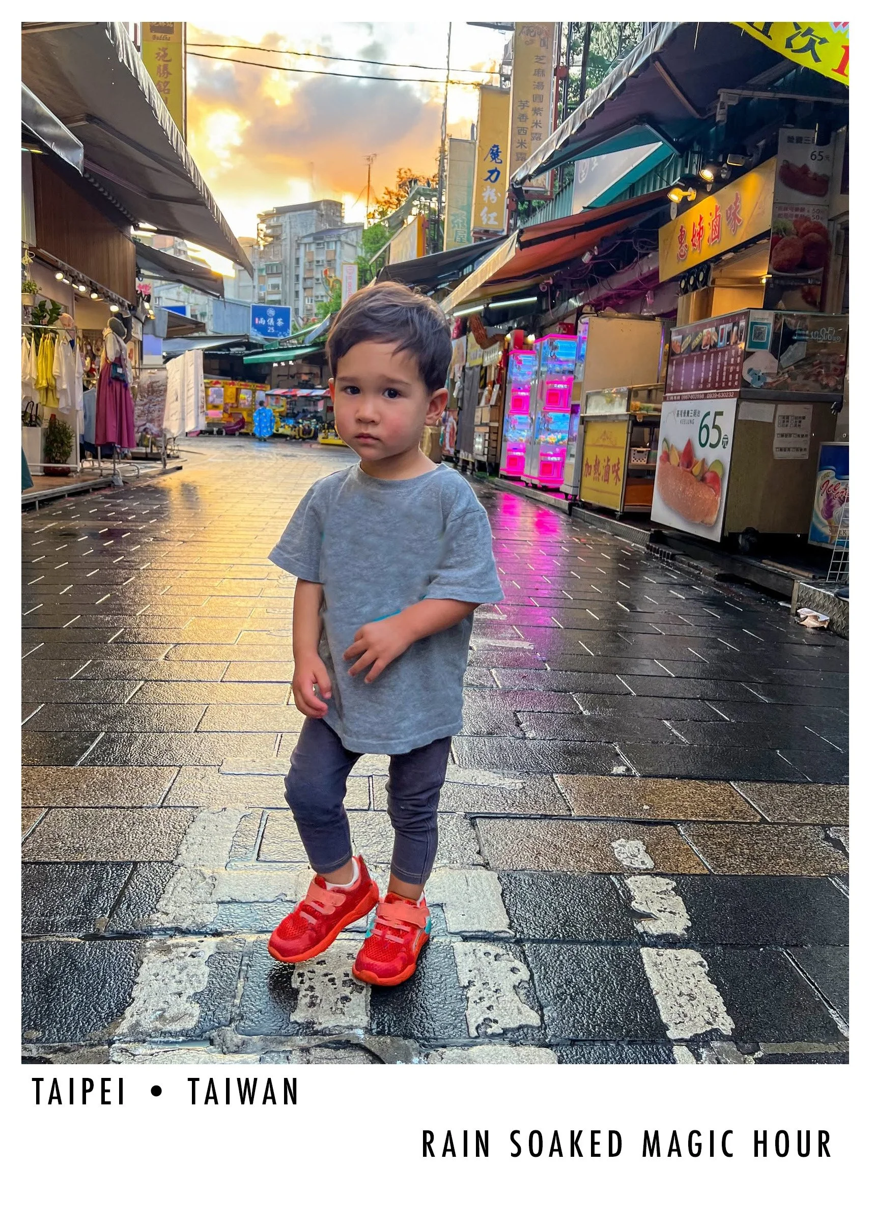 A young boy wearing red sneakers and a gray t-shirt standing on a wet, nighttime street in Taipei, Taiwan, with shops and neon signs in the background and a colorful sunset sky above.