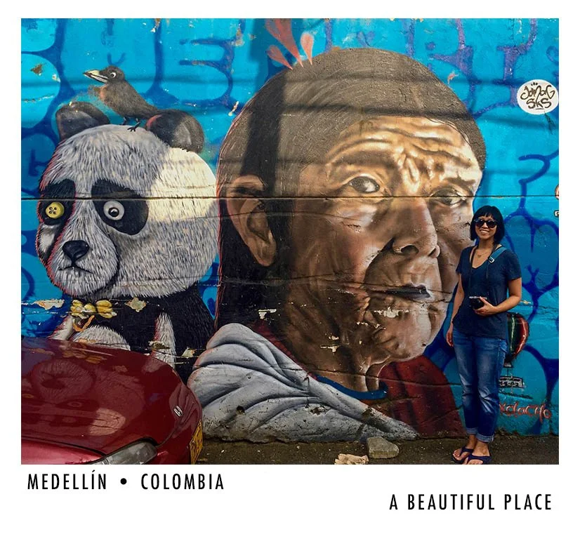 Colorful mural in Medellín, Colombia, featuring a detailed portrait of a man's face, a panda with a bird on its head, and a woman standing in front of the mural.