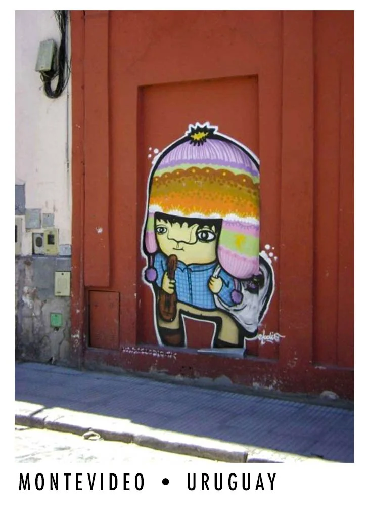 Street art graffiti of a cartoon girl wearing a large multicolored knit hat, a blue shirt, and holding a brown ice cream cone, painted on a red wall in Montevideo, Uruguay.