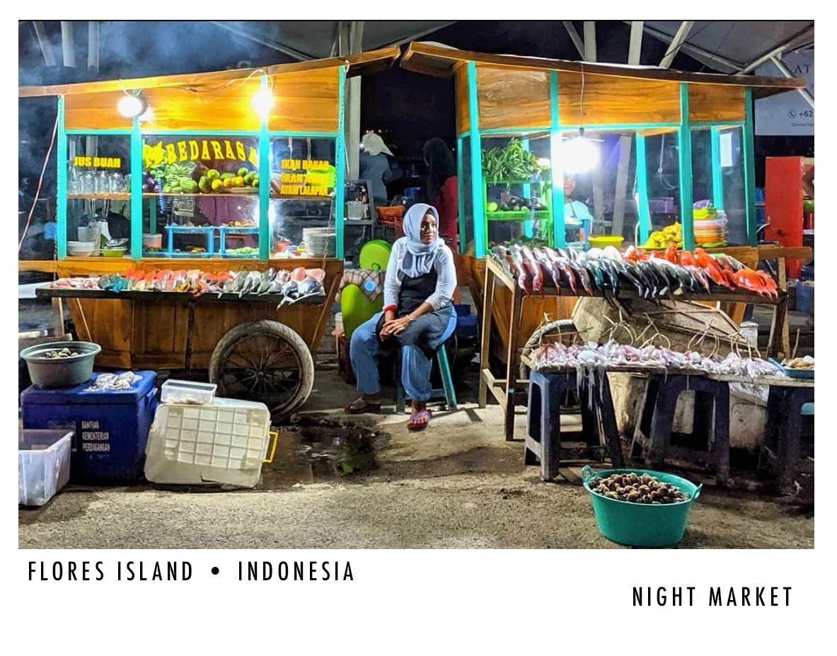Night market stall on Flores Island, Indonesia, selling fresh seafood including fish and shellfish, with a woman sitting in front of the stall.