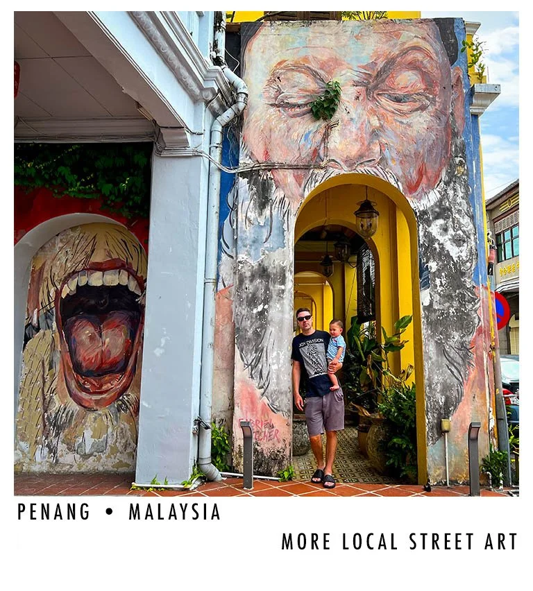 Colorful street art murals of a large face with closed eyes above an arched doorway, and a wide-open-mouth scream on a wall to the left, on a building in Penang, Malaysia.