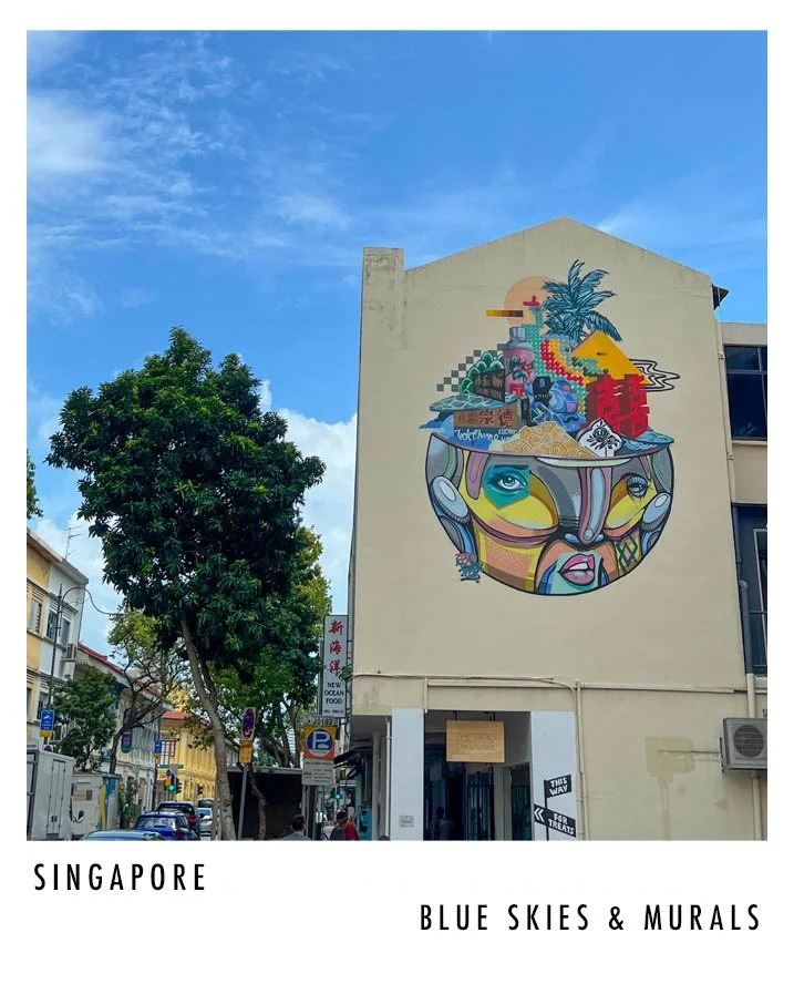 Colorful mural on the side of a building in Singapore, depicting a surreal face with vibrant abstract elements, palm trees, and cityscape.