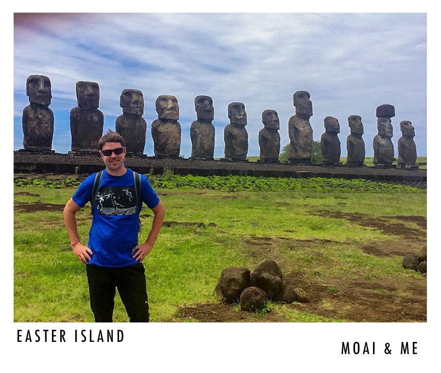 A young man in sunglasses and a blue T-shirt standing in front of moai statues on Easter Island, with green grass and cloudy sky in the background.