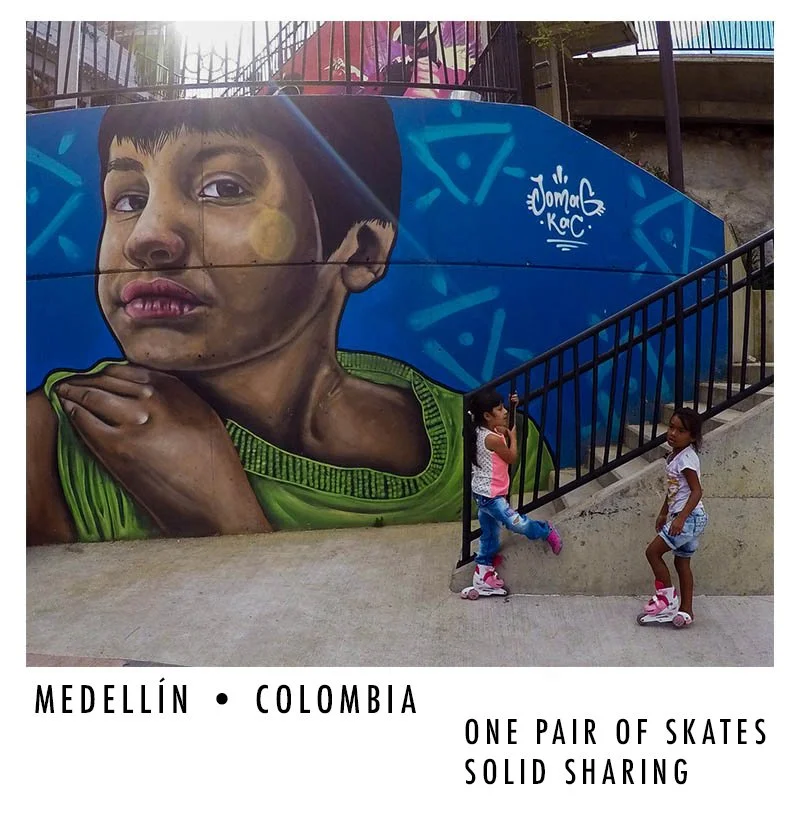 Street art mural of a young boy with a thoughtful expression, green shirt, on a wall next to two children wearing roller skates.