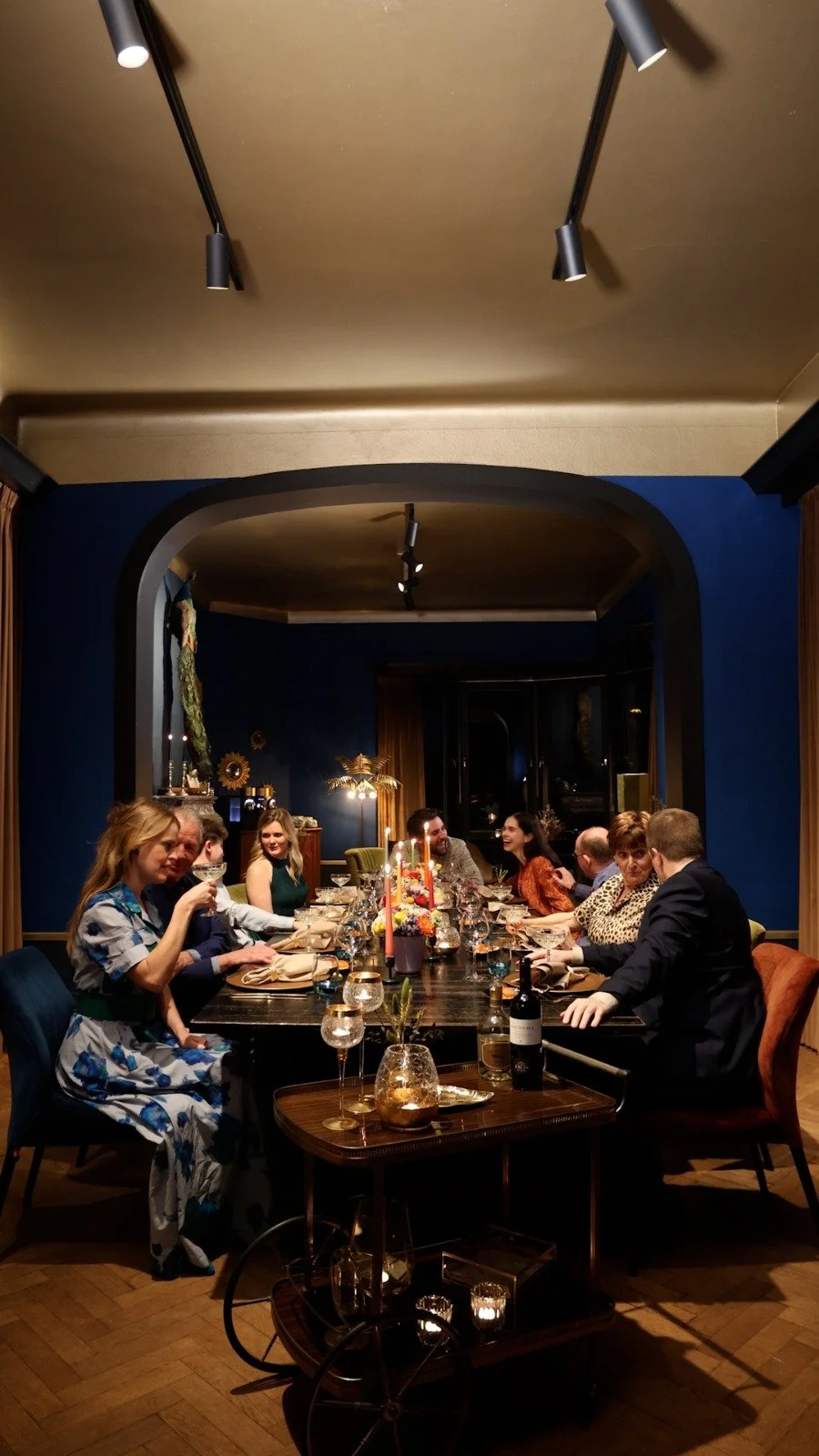 Groep mensen staan in een kring buiten 's nachts, verlicht door een roodachtig licht, met bomen op de achtergrond.
