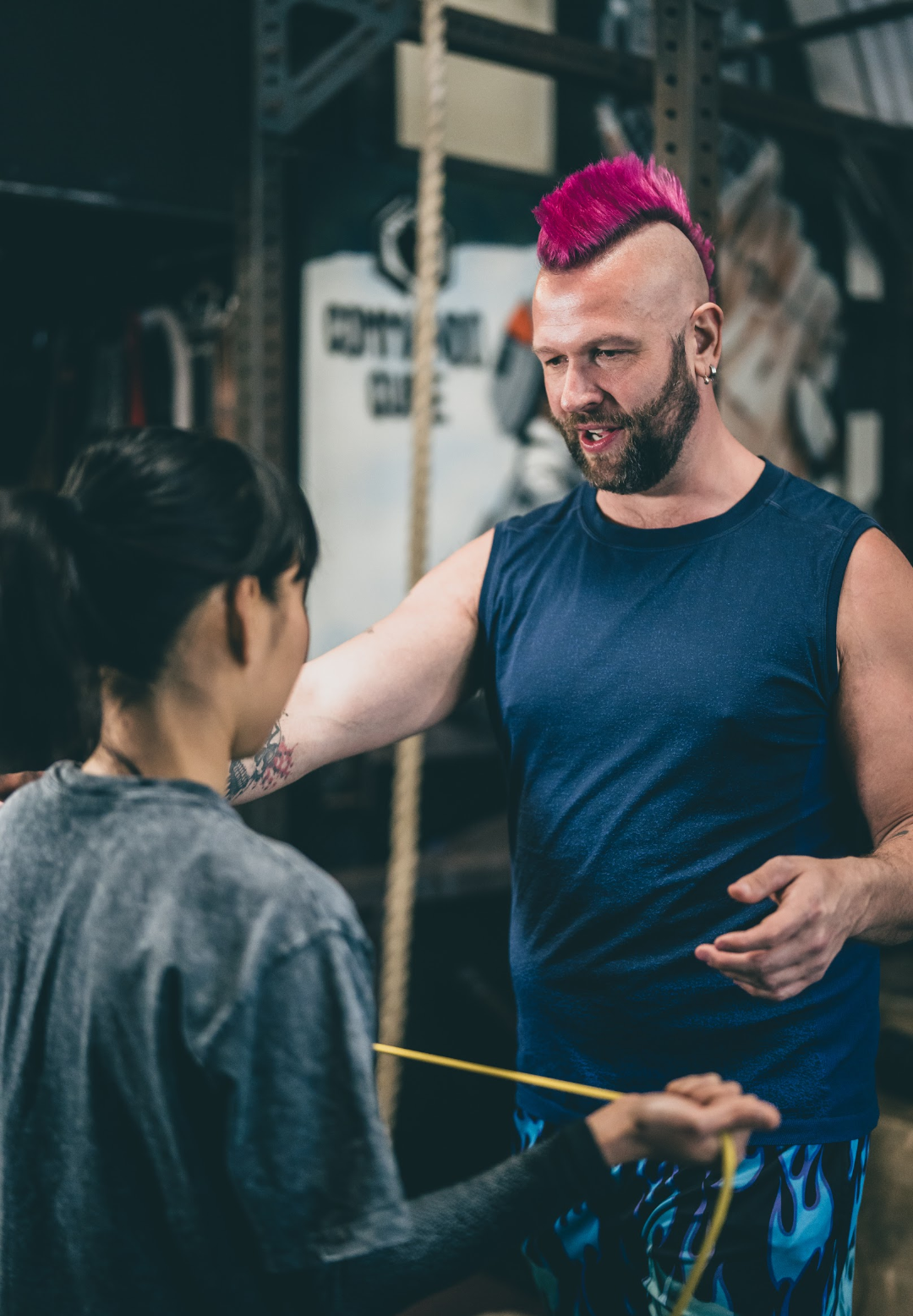 A man with a pink mohawk showing a female client fascia informed movements for shoulder recovery.