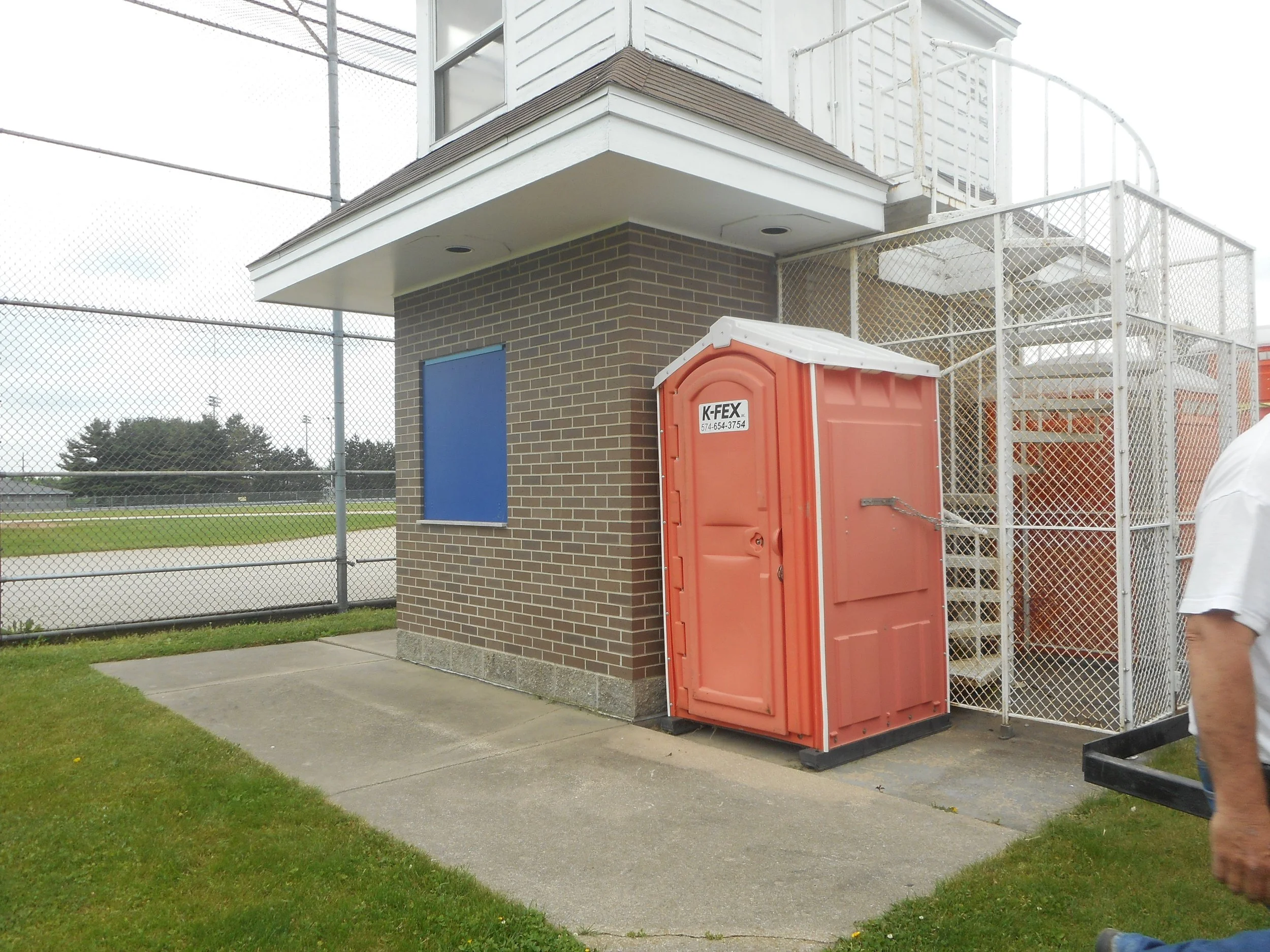 A K-FEX portable toilet next to a school soccer field and bleachers