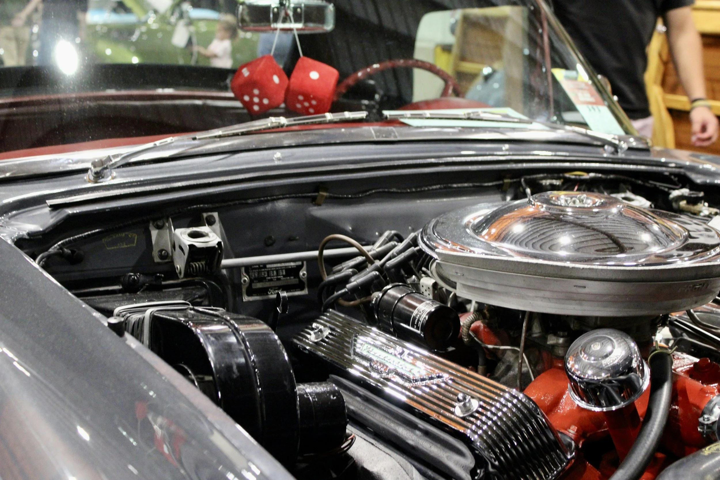 A mechanic in a black and gray jacket filling the engine oil of a car with a container labeled Mobil 1.