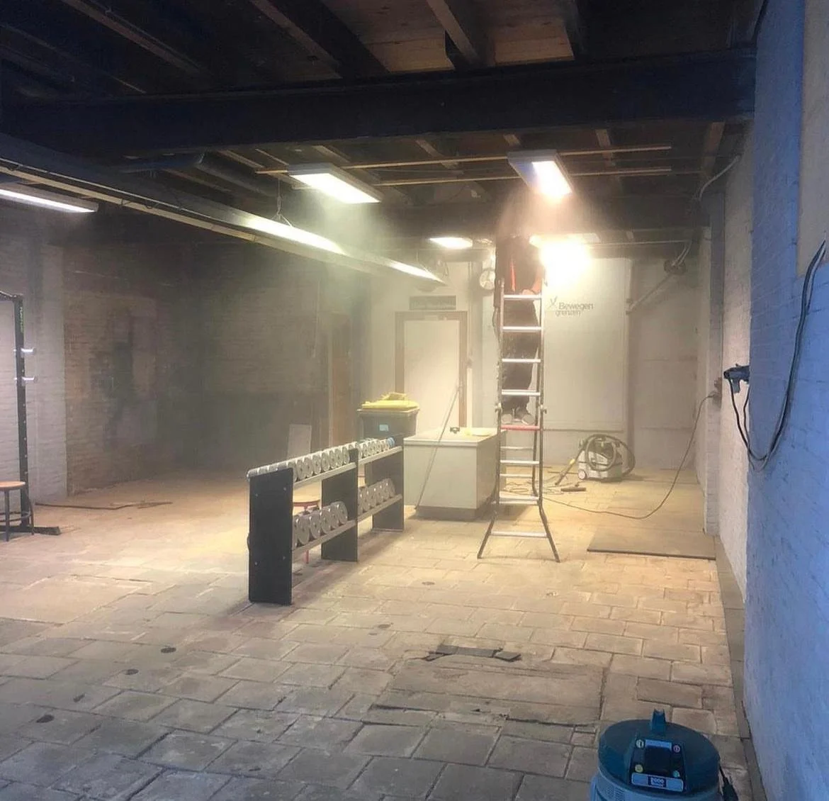 Binnenruimte onder grote renovatie of bouw, met stof, ladder en bouwmaterialen.