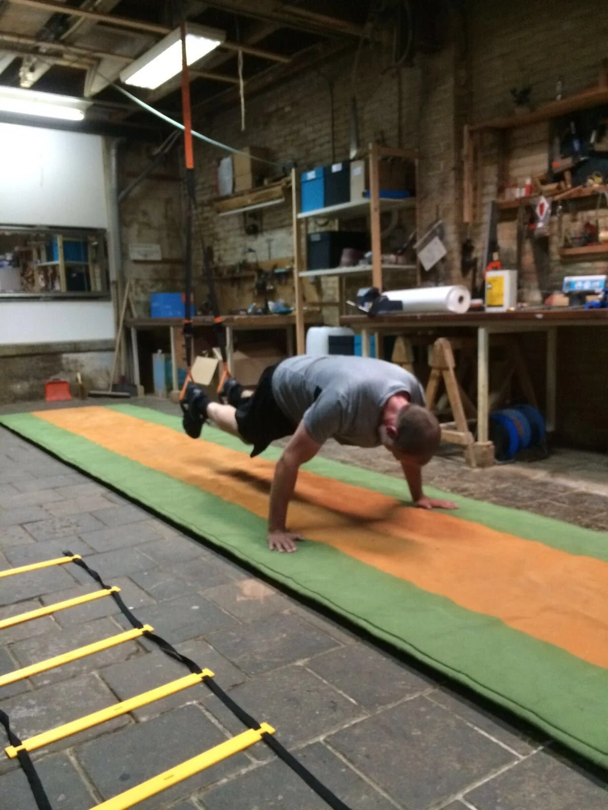 Man die een planken plank balanceert op handen en voeten op een mat in een garage-werkplaats.