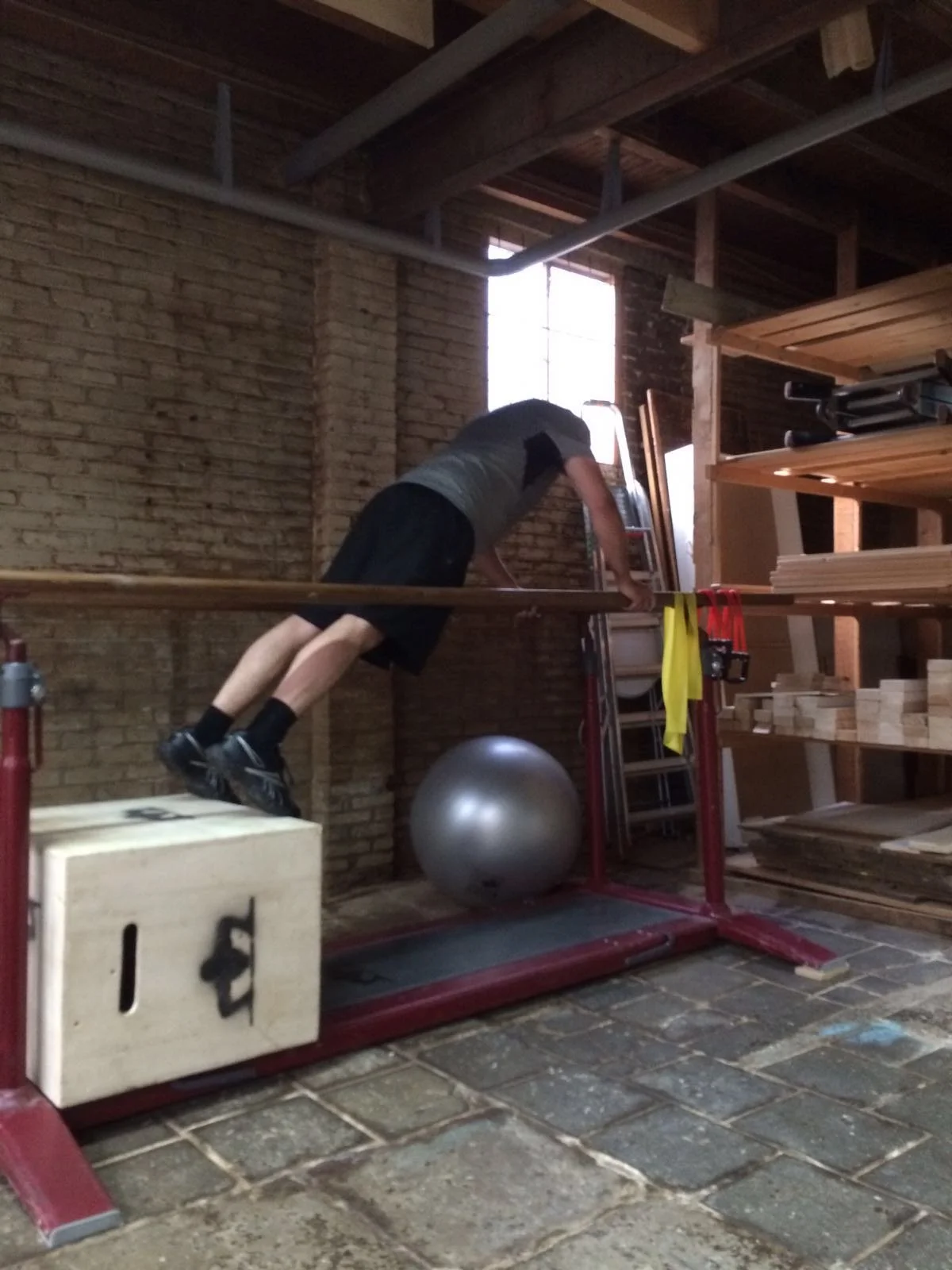 Man die op een houten bankje in een werkplaats een oefening uitvoert met een stability bal en houten plank.