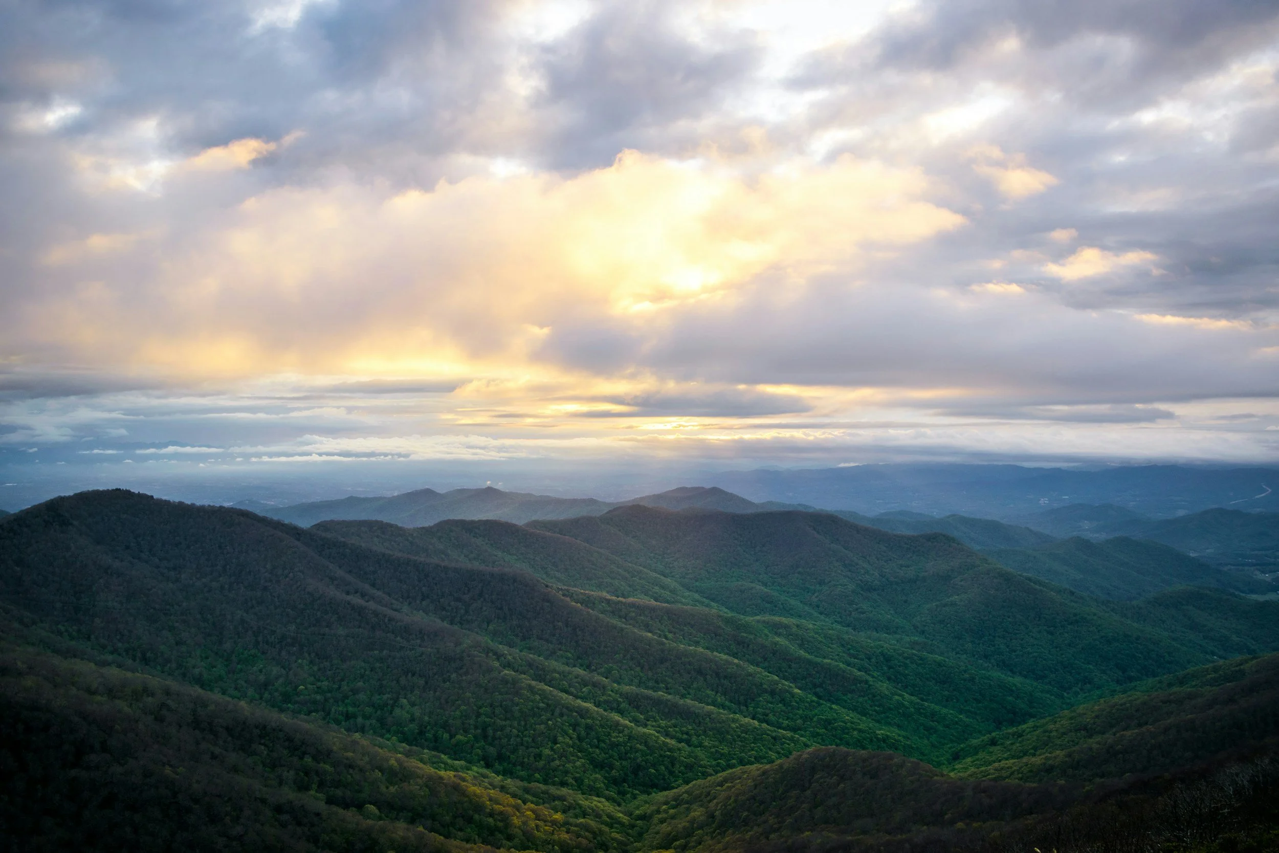 Scenic view of rolling green mountains under a cloudy sky with sunlight breaking through the clouds.
