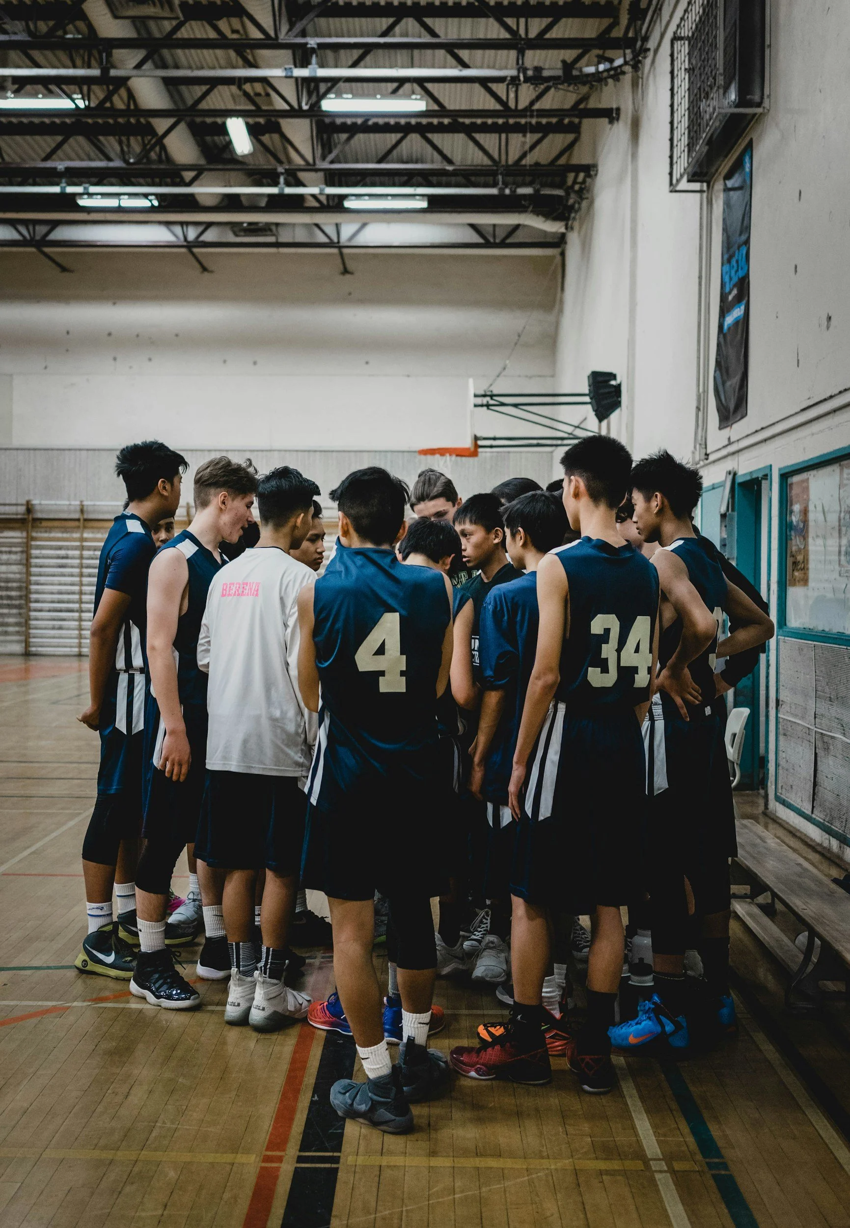 A basketball team huddles together on an indoor court, possibly during a timeout or team talk.