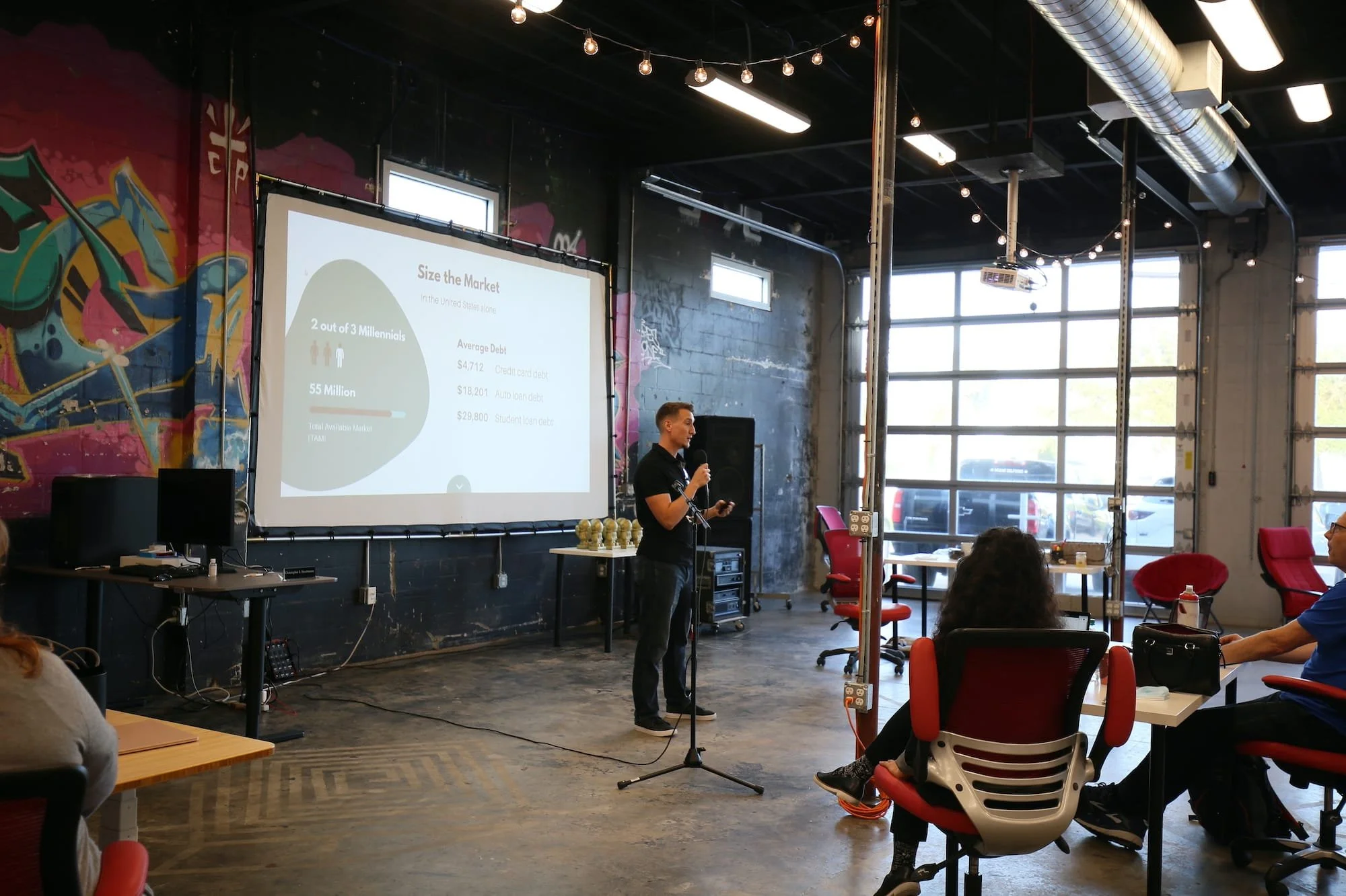 Image of a man in front of a projection screen speaking to a crowd in a coffee shop setting