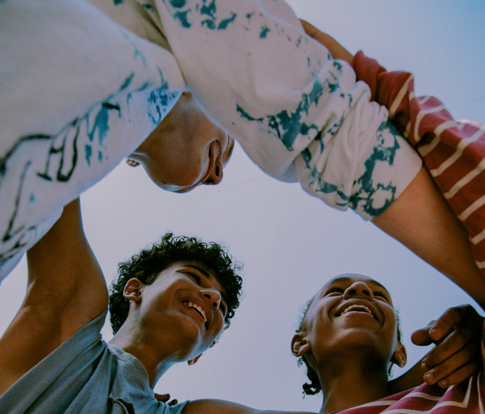 Four friends hold hands in a circle, smiling and looking down at the camera.