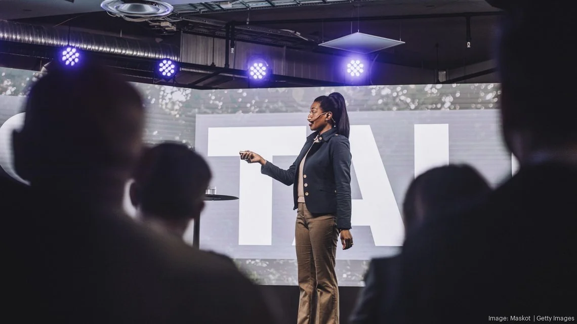 Image of a woman speaking to a crowd with a headset and purple lights shining on her