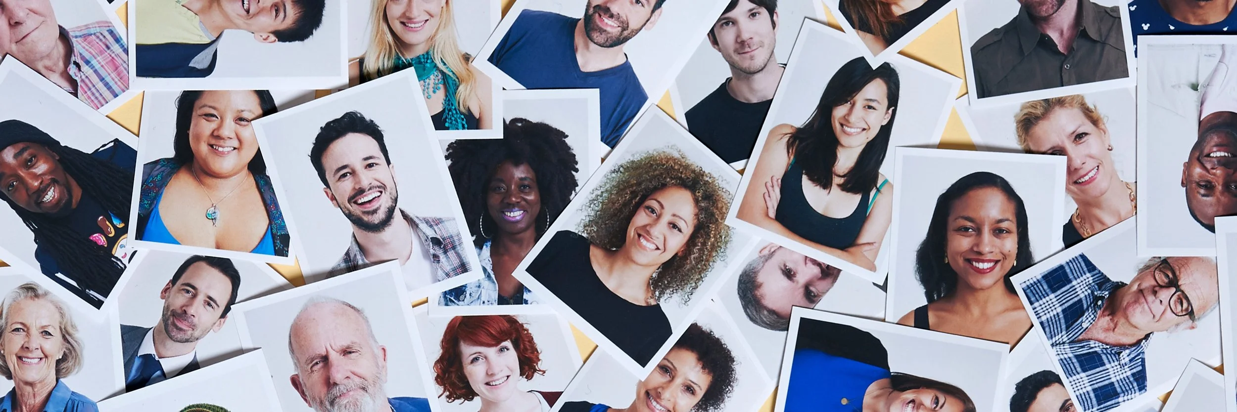 A collection of assorted printed photographs of diverse smiling people in various poses, scattered on a flat surface.