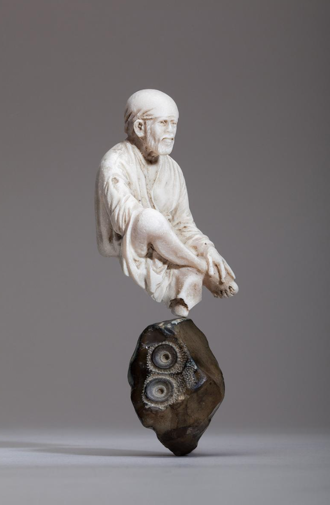 Alabaster figurine of the Indian spiritual master, Sai Baba (d. 1918), circa 20th century; balanced on a Jurassic period fossilised sea urchin, 'echinoid cidaris'. Photo: Hannah Smiles