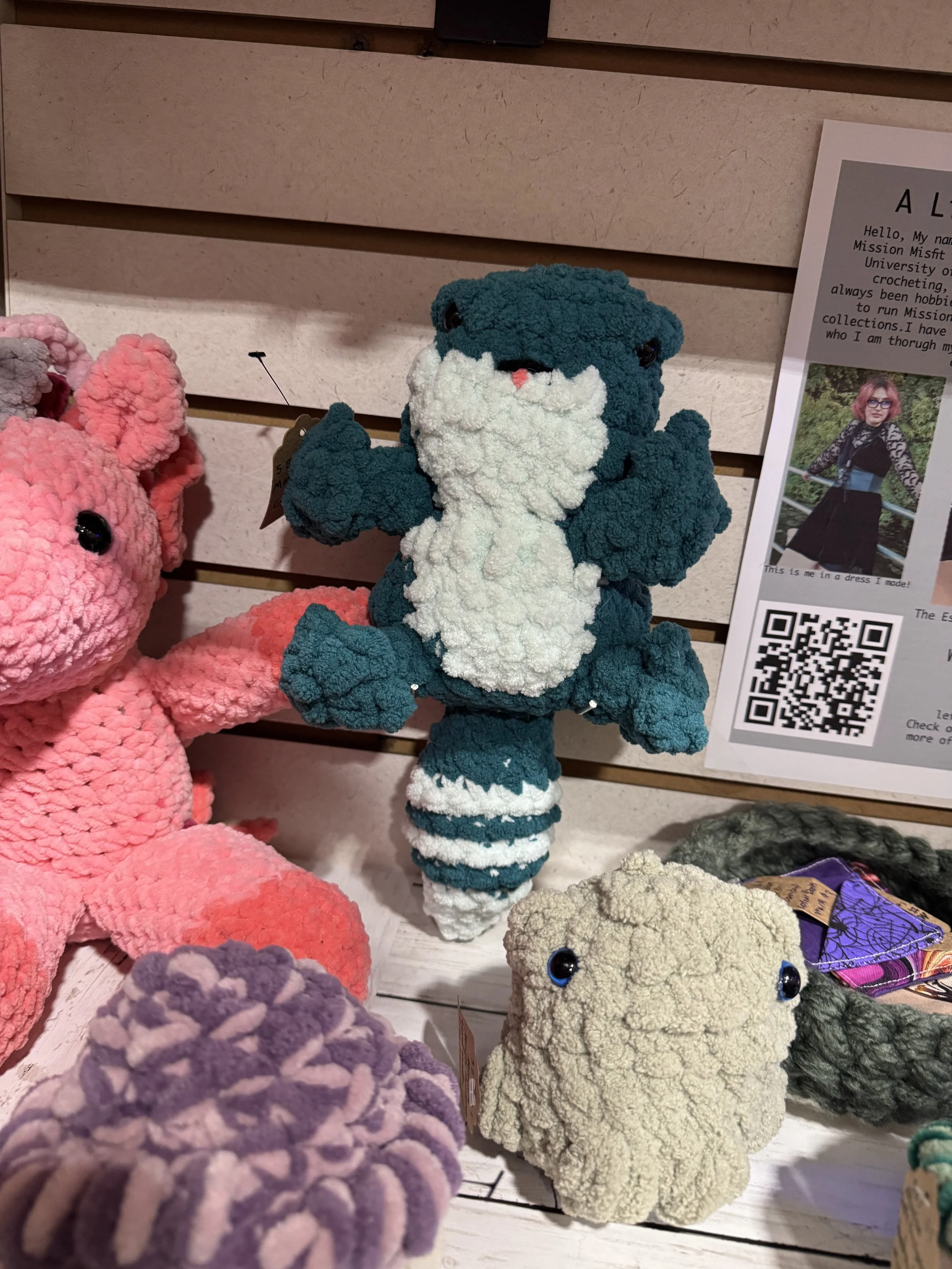 A teal and white plush crocodile stuffed toy surrounded by other plush animals on a store shelf.