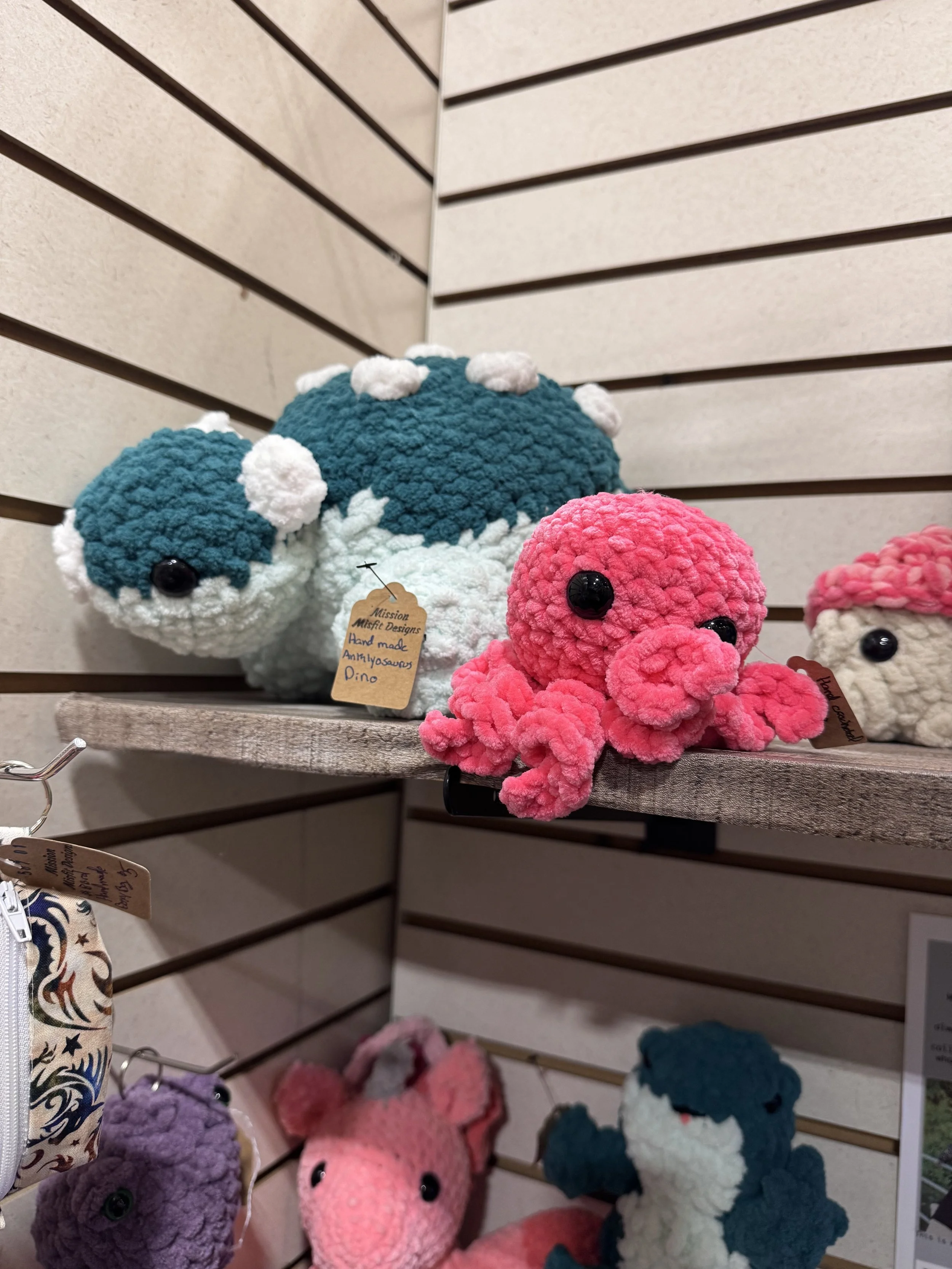 Colorful plush toys, including a pink octopus and a blue and white dinosaur, displayed on shelves in a store.