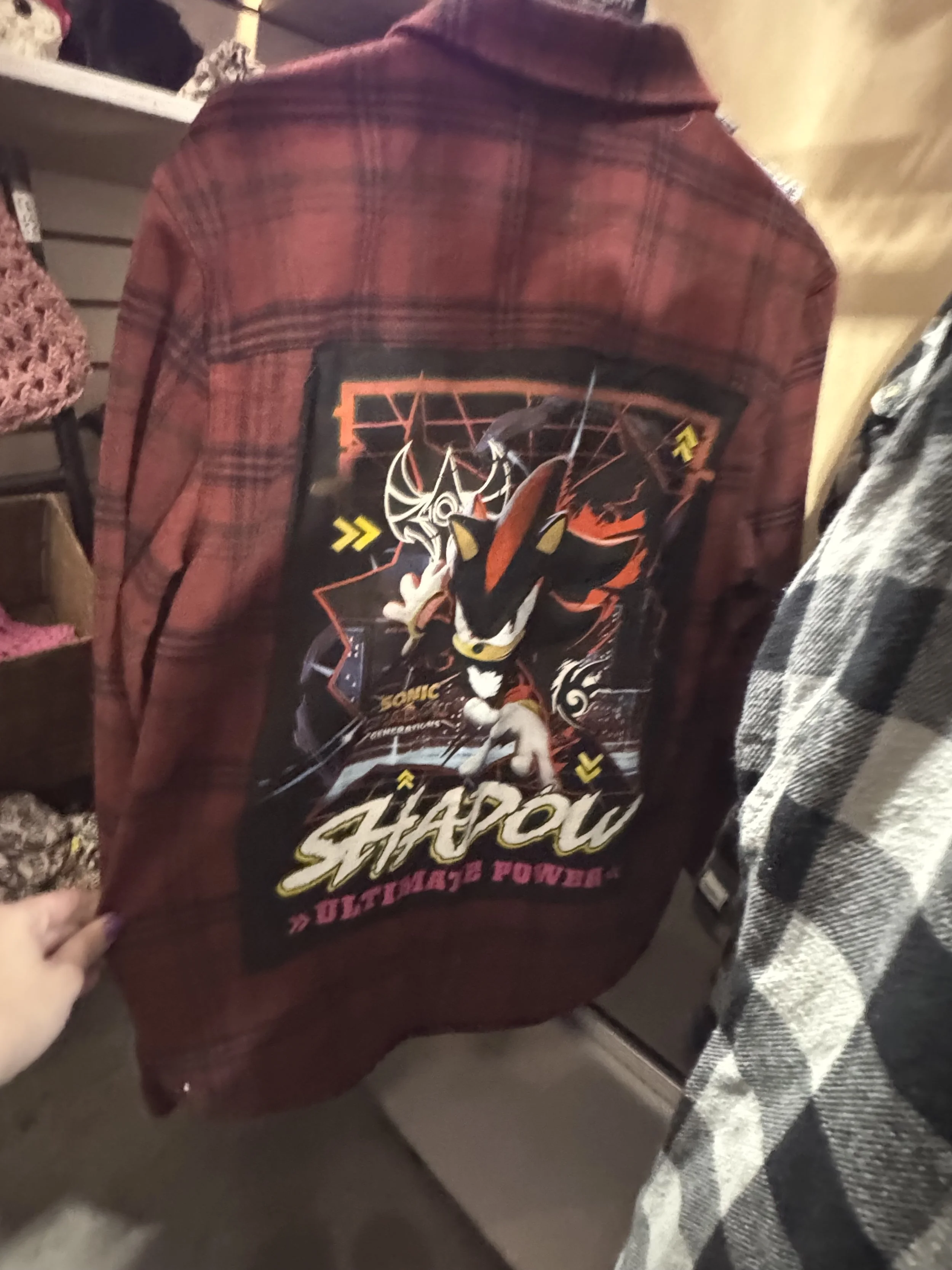 A person wearing a red plaid jacket with a large graphic on the back featuring Sonic the Hedgehog and Shadow, with the words 'Shadow' and 'Ultimate Power'.