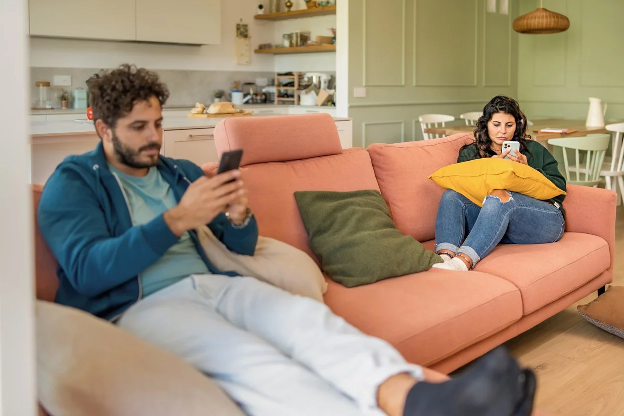 Married couple sitting apart on a couch, emotionally distant, a sign of roommate syndrome.