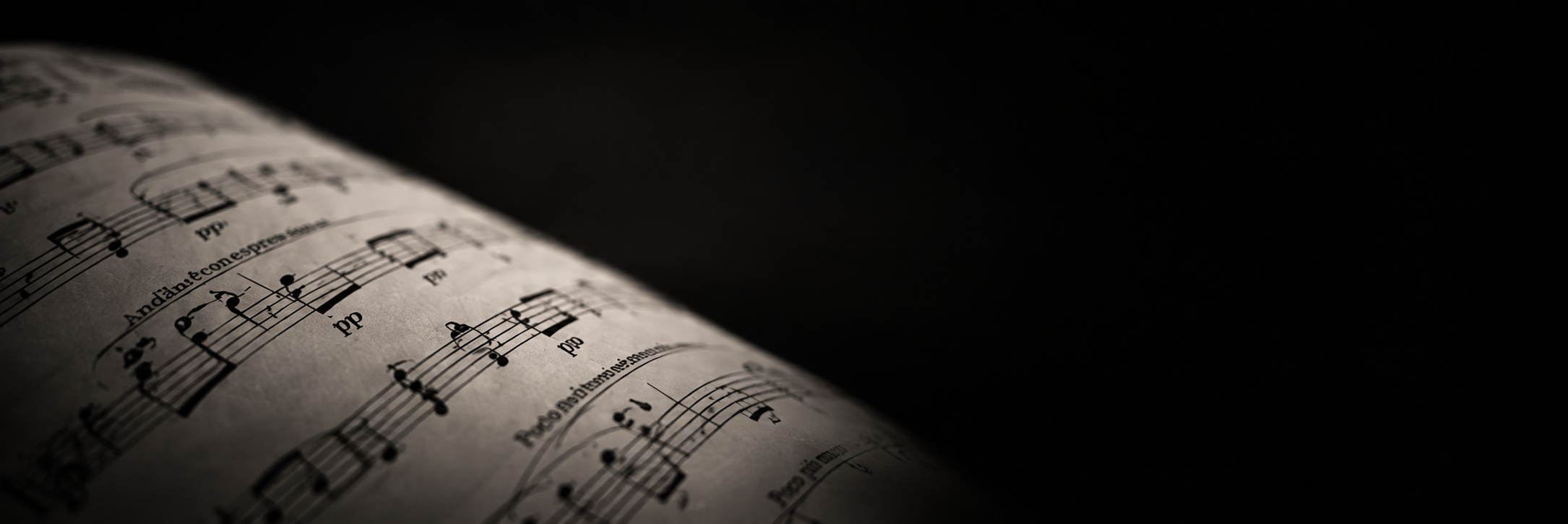 Close-up of printed sheet music with musical notes, clefs, and annotations, illuminated with soft lighting against a dark background.