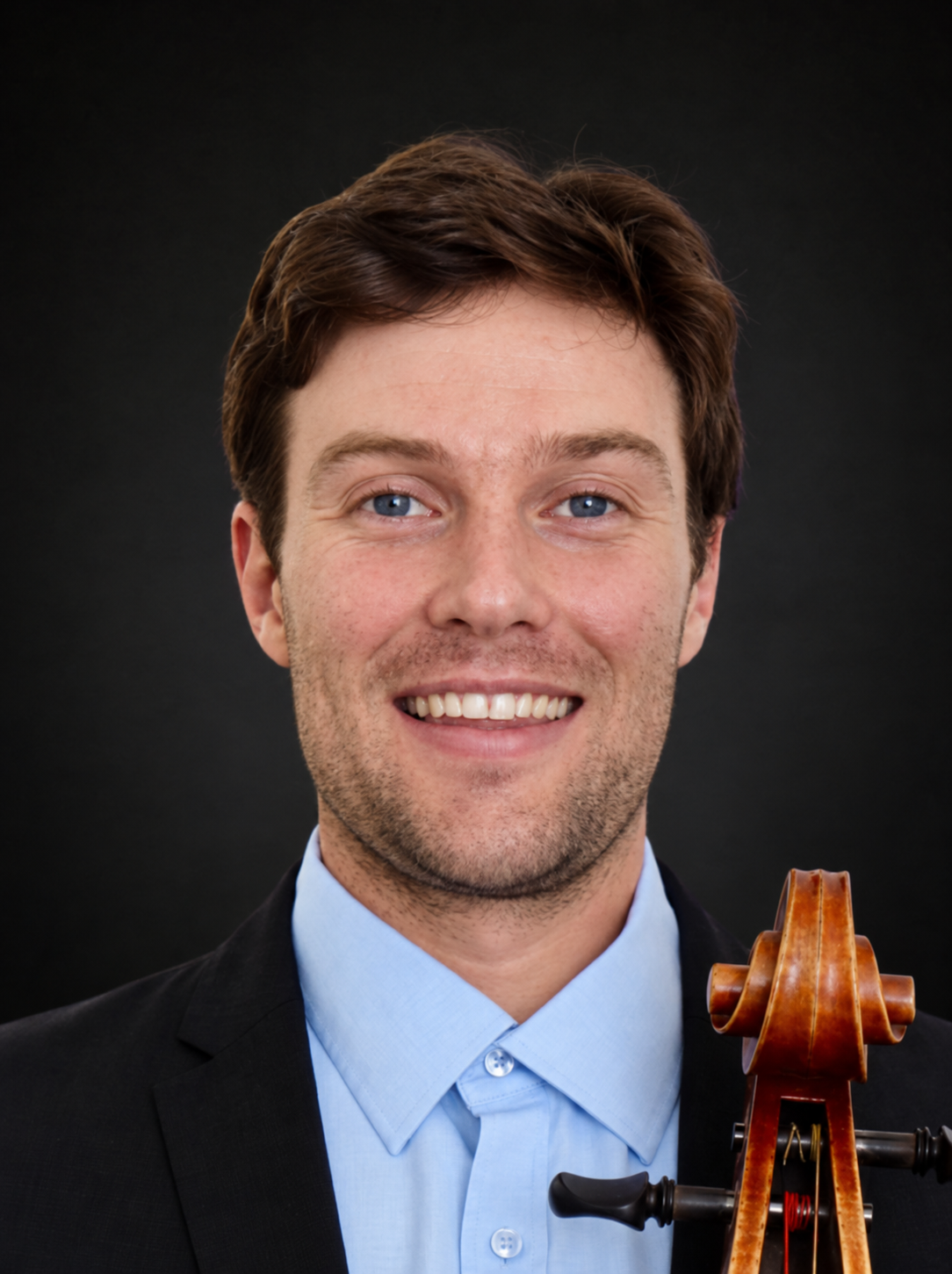A man with light skin, blue eyes, and brown hair smiling at the camera, wearing a black suit and light blue shirt, with a violin on his shoulder.