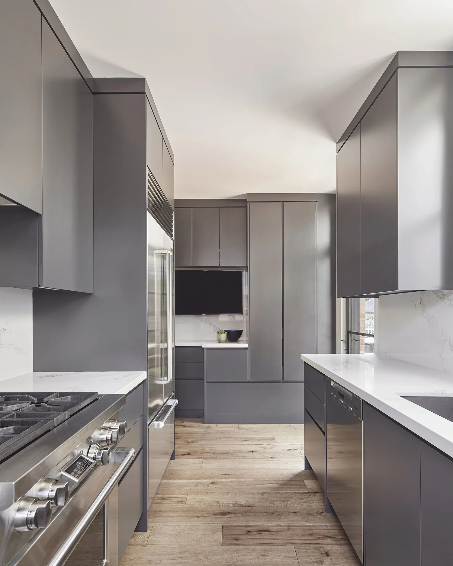 Modern kitchen with gray cabinets, white countertops, stainless steel appliances, and light wood flooring.