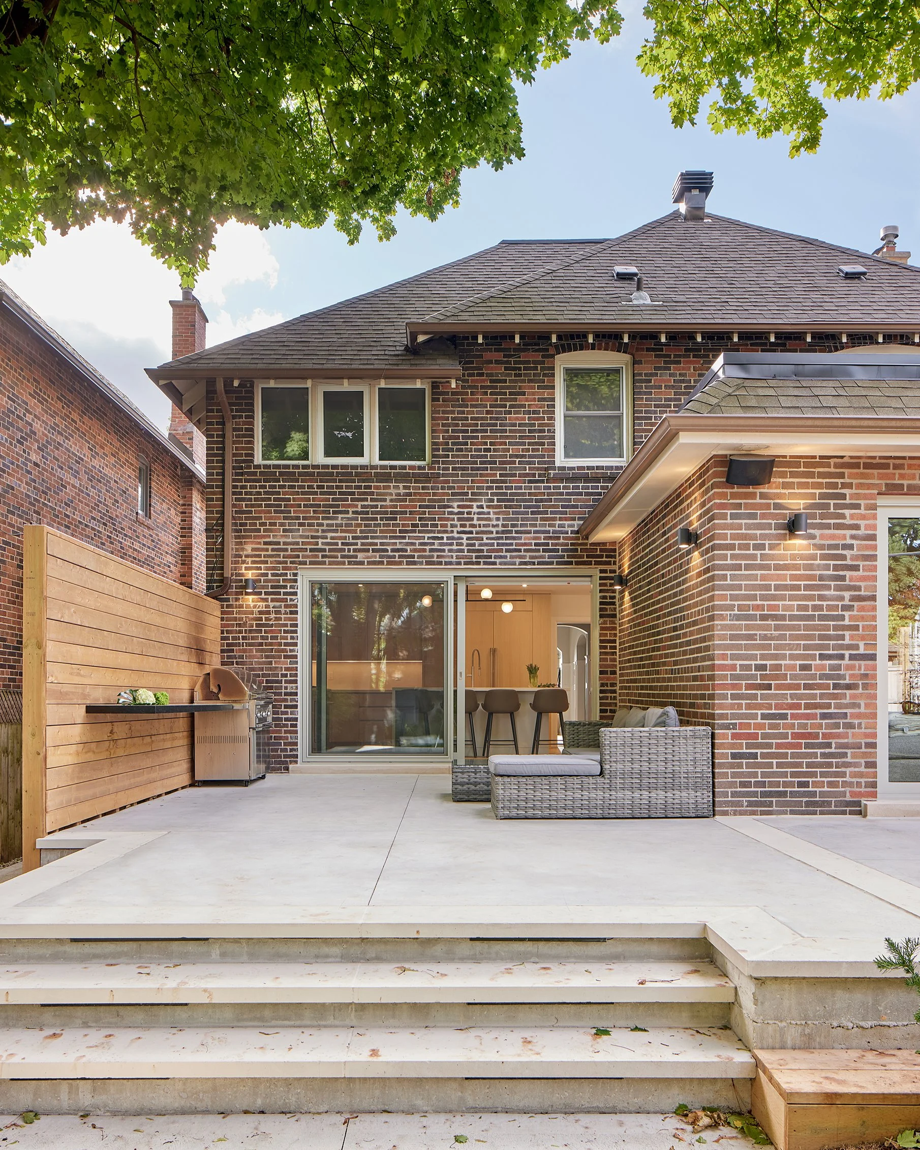 Backyard patio of a brick house with outdoor seating, a grill, and sliding glass door leading inside.