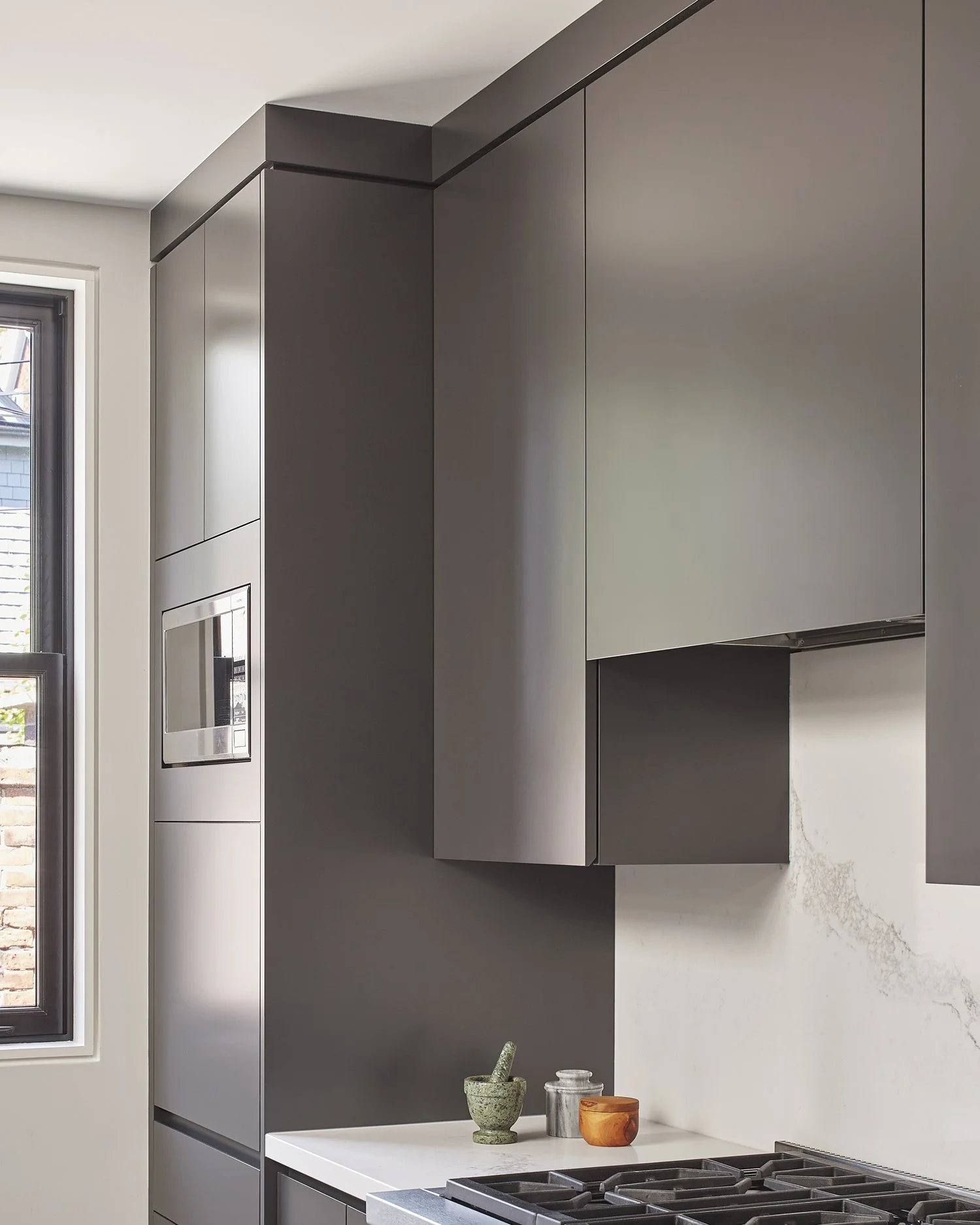 Modern kitchen with dark gray cabinets, a white marble backsplash, and a gas stove. A window provides natural light.