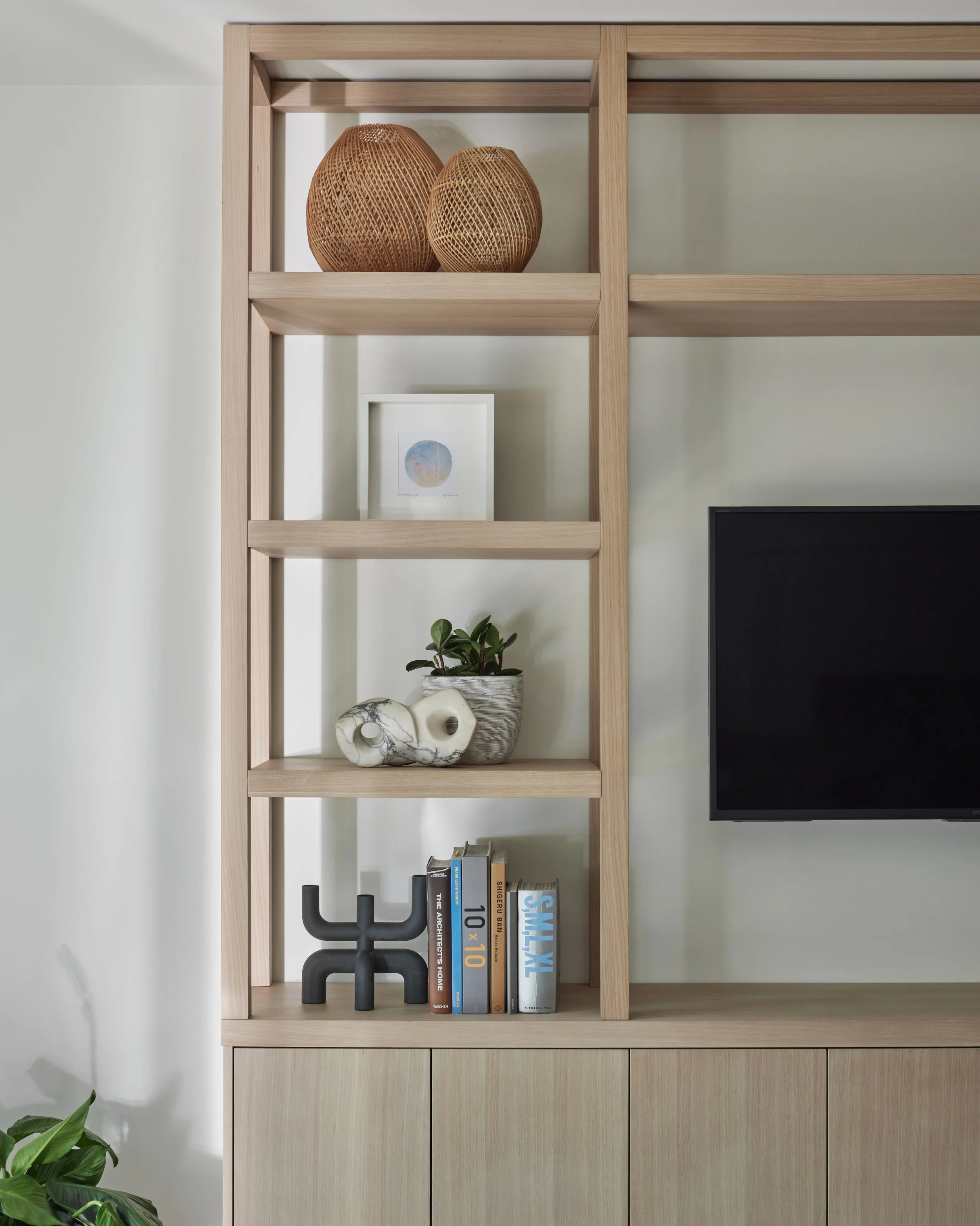 A wooden shelving unit with decorative vases, framed artwork, a potted plant, abstract sculpture, a row of books, and a black TV on a light green wall.