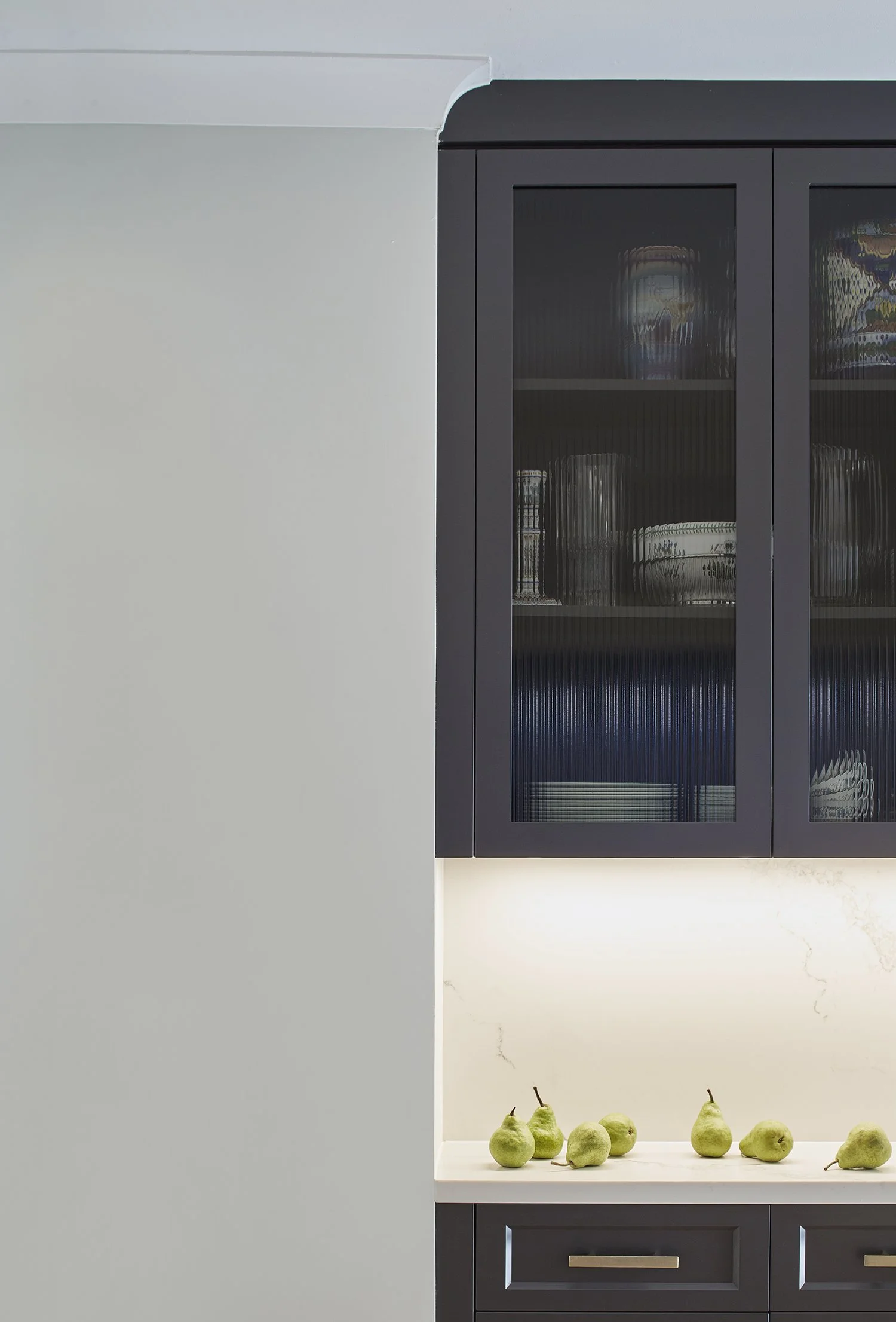 Kitchen cabinet with glass doors above a white countertop with pears arranged on it.