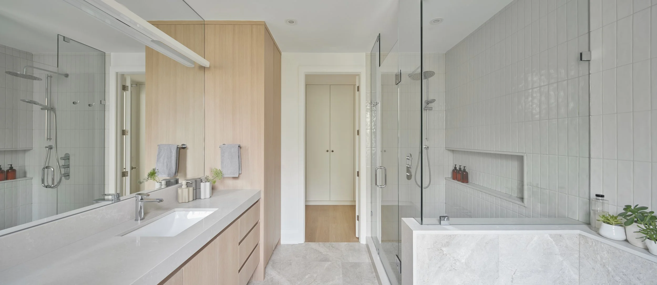 Modern bathroom with a double vanity, large mirror, and two walk-in showers with glass doors and tiled walls, decorated with potted plants and toiletries.