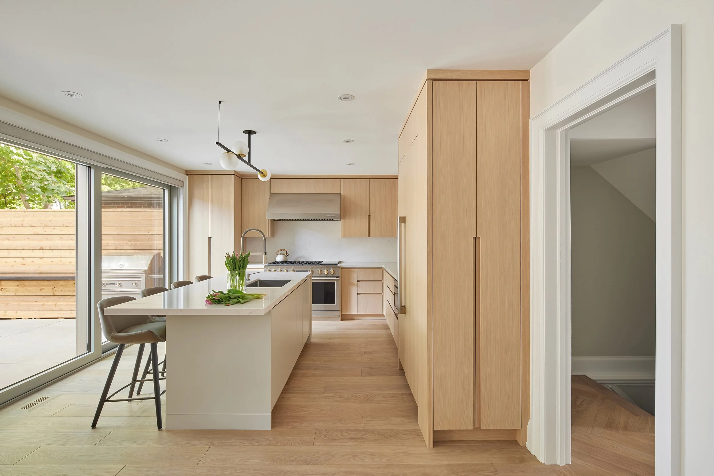 Modern kitchen with light wood cabinets, white island, stainless steel appliances, and large sliding glass door leading to patio.