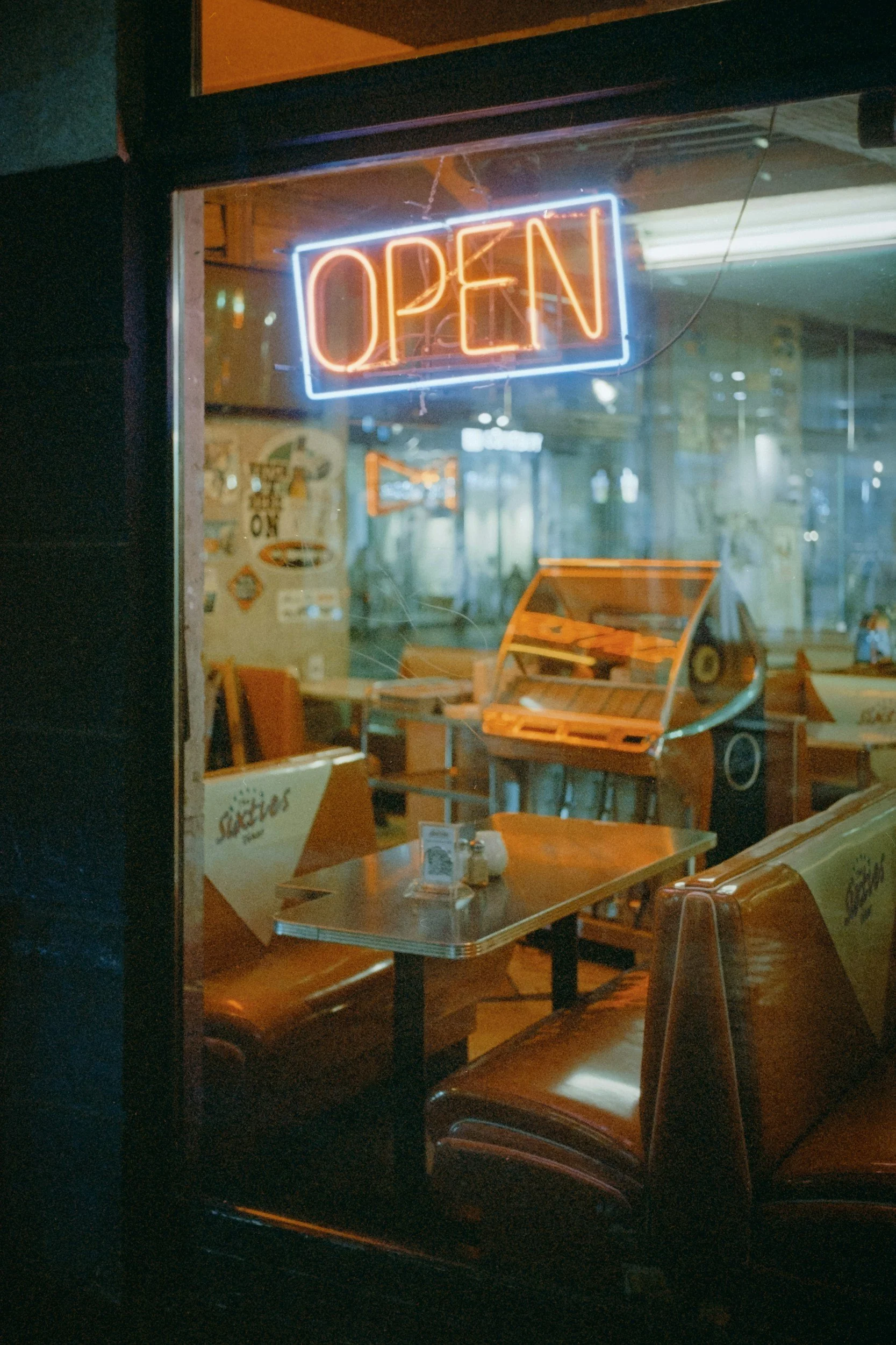 Neon sign displaying 'OPEN' inside a restaurant or cafe with visible booths and a jukebox