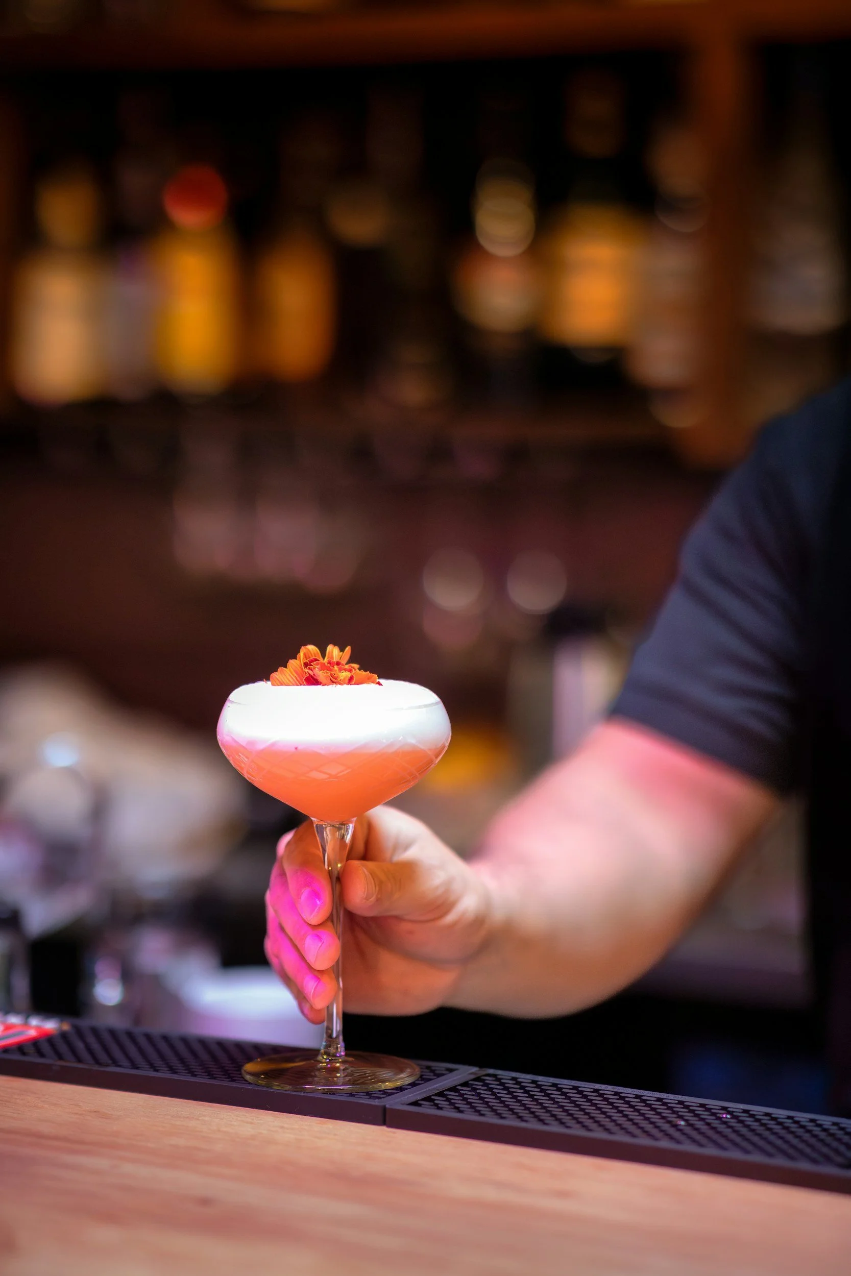 bartenders hand passing over a cocktail with a flower on top