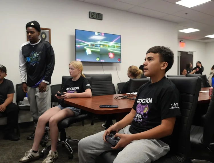 Young players using game controllers with a KAYGE team member nearby