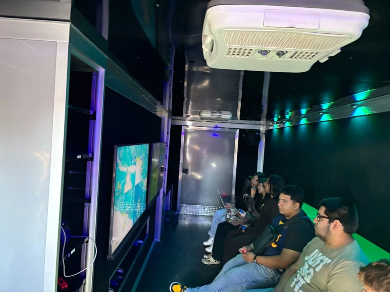People sitting in a dark room watching screens, with air conditioning unit on the ceiling.
