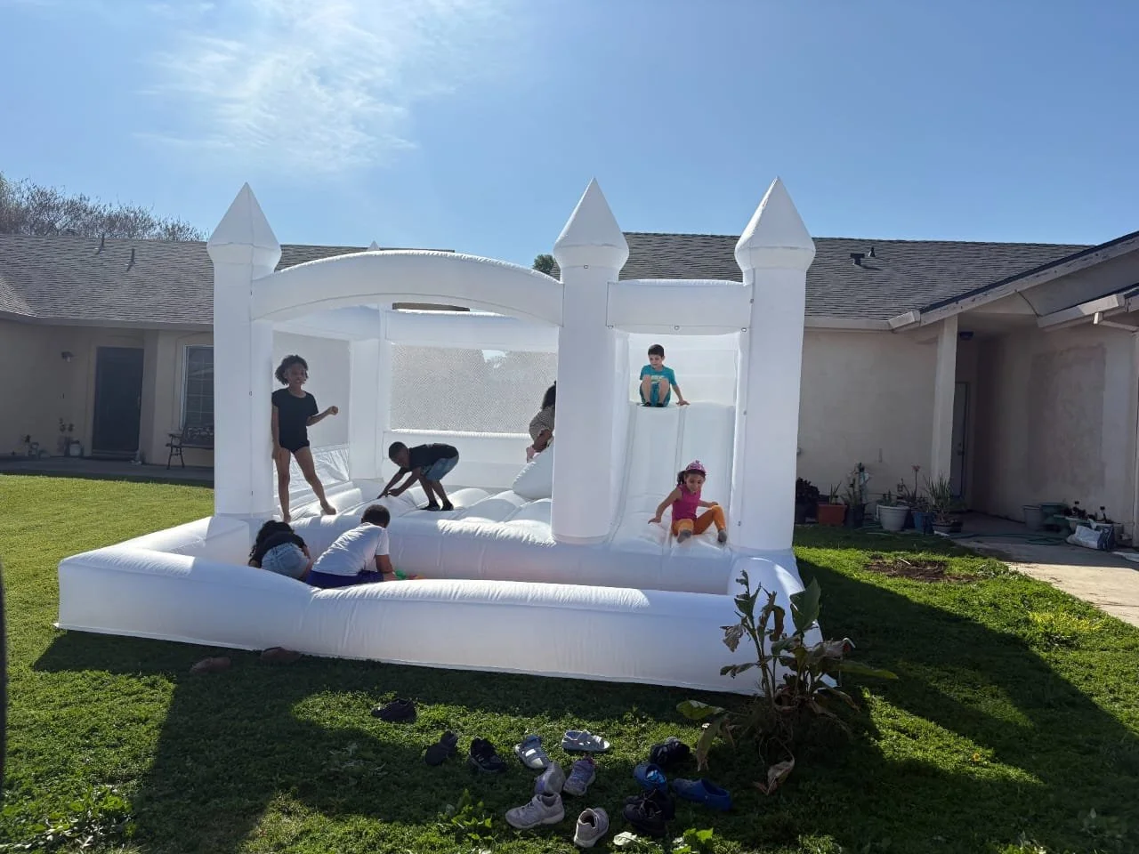 Children playing on a large white inflatable castle with turrets in a backyard.