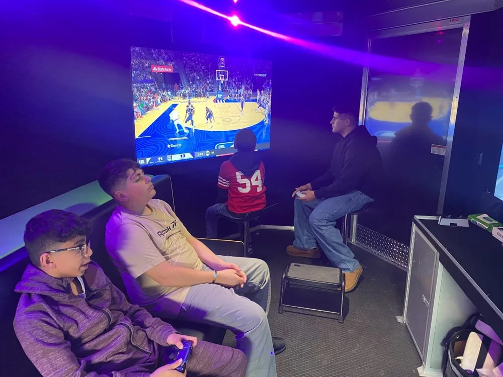 Young players using game controllers with a KAYGE team member nearby