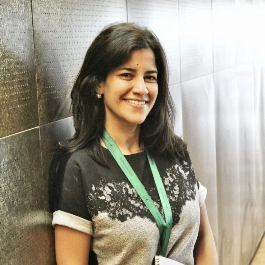 Professional woman with dark hair wearing a black blazer, pearl necklace, and pearl earrings, smiling at the camera against a plain background.
