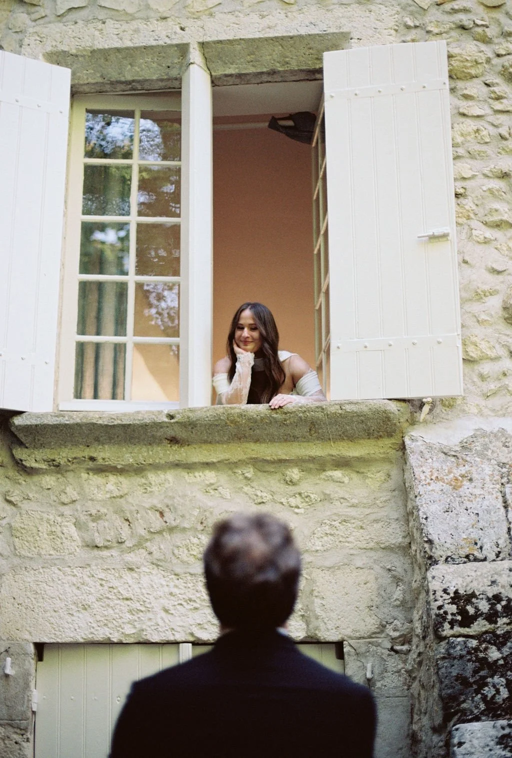 A woman looking out of an open window and smiling at a man who is standing outside with his back to the camera.
