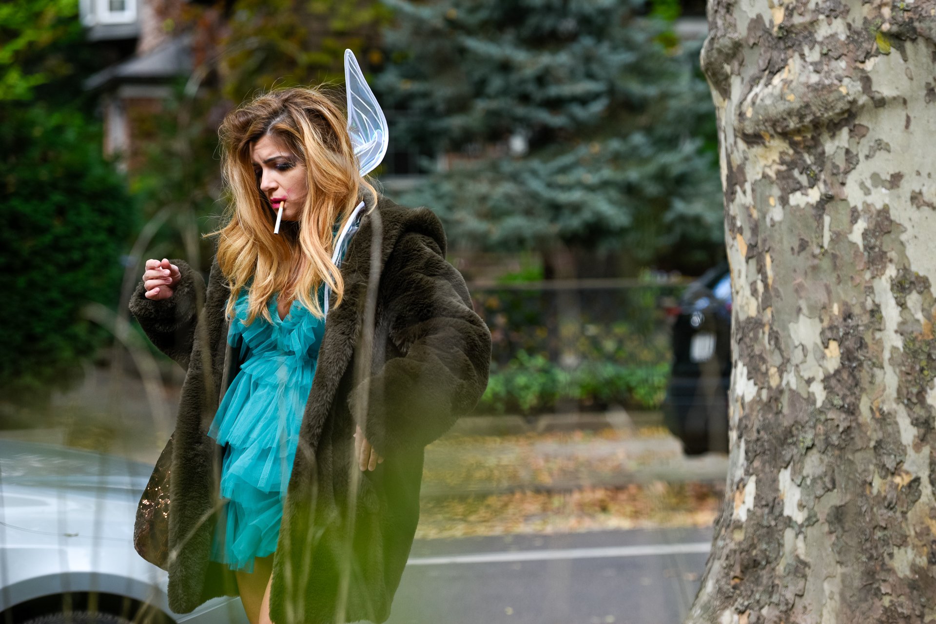 Woman smoking in a fuzzy coat with a fairy wing sticking out