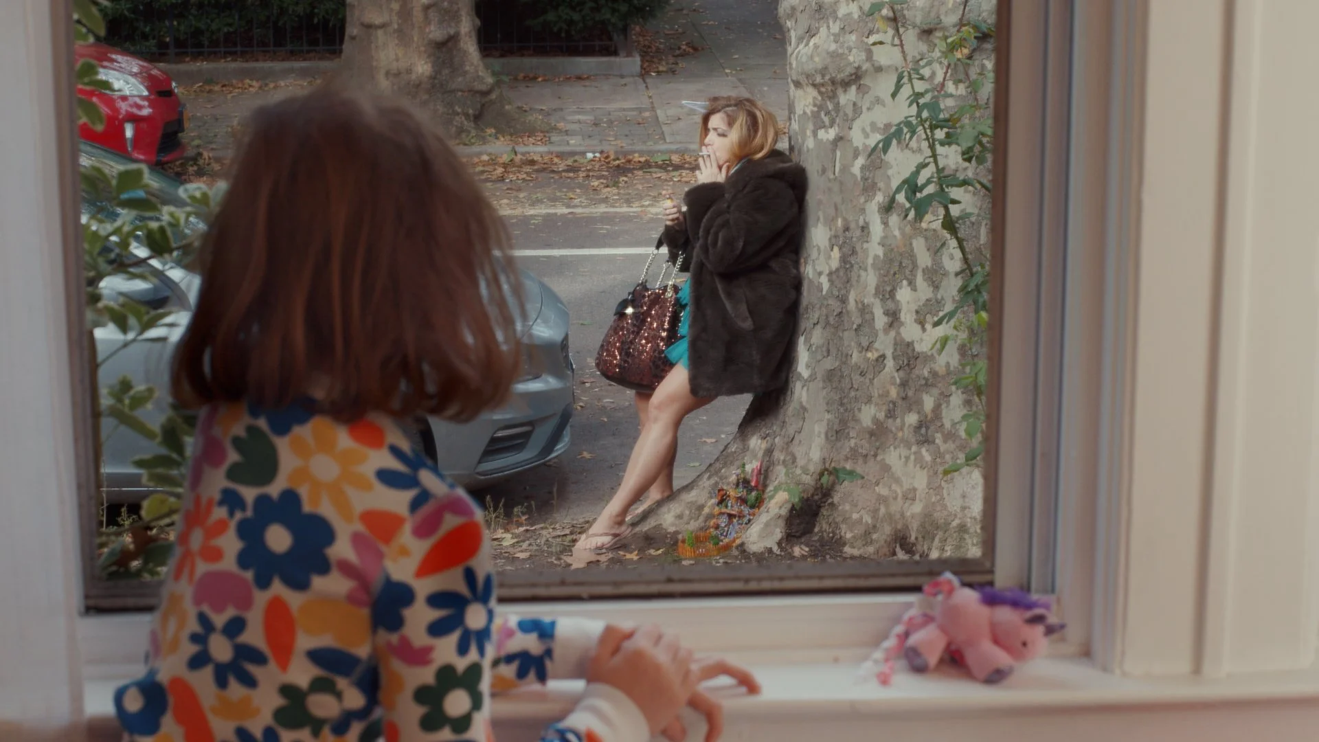 Young girl watches through the window at a grown woman smoking a cigarette