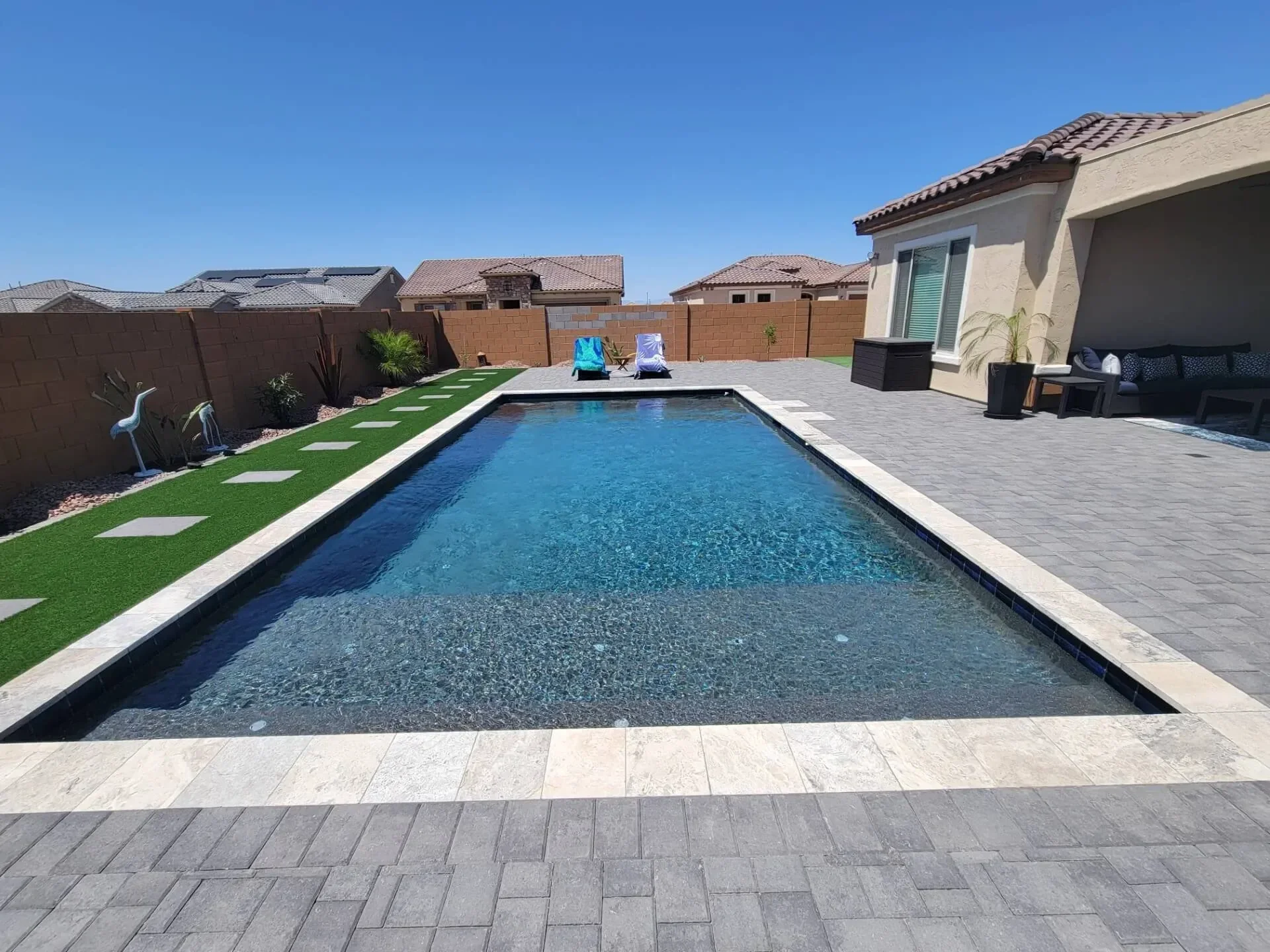 Backyard with swimming pool, patio furniture, and decorative lawn accents under a clear blue sky.