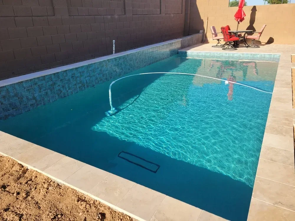 Backyard patio with swimming pool, pool cleaning hose, and patio furniture under a red umbrella.