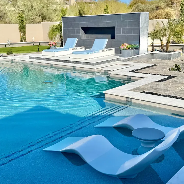 Luxury outdoor swimming pool area with modern loungers and a water feature, surrounded by sleek landscaping and plants.