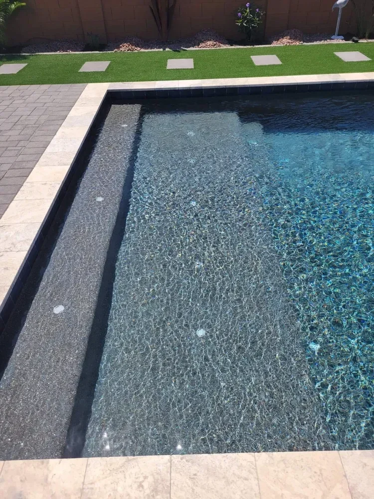 Swimming pool with clear water, stone decking, and adjacent artificial grass with stepping stones.